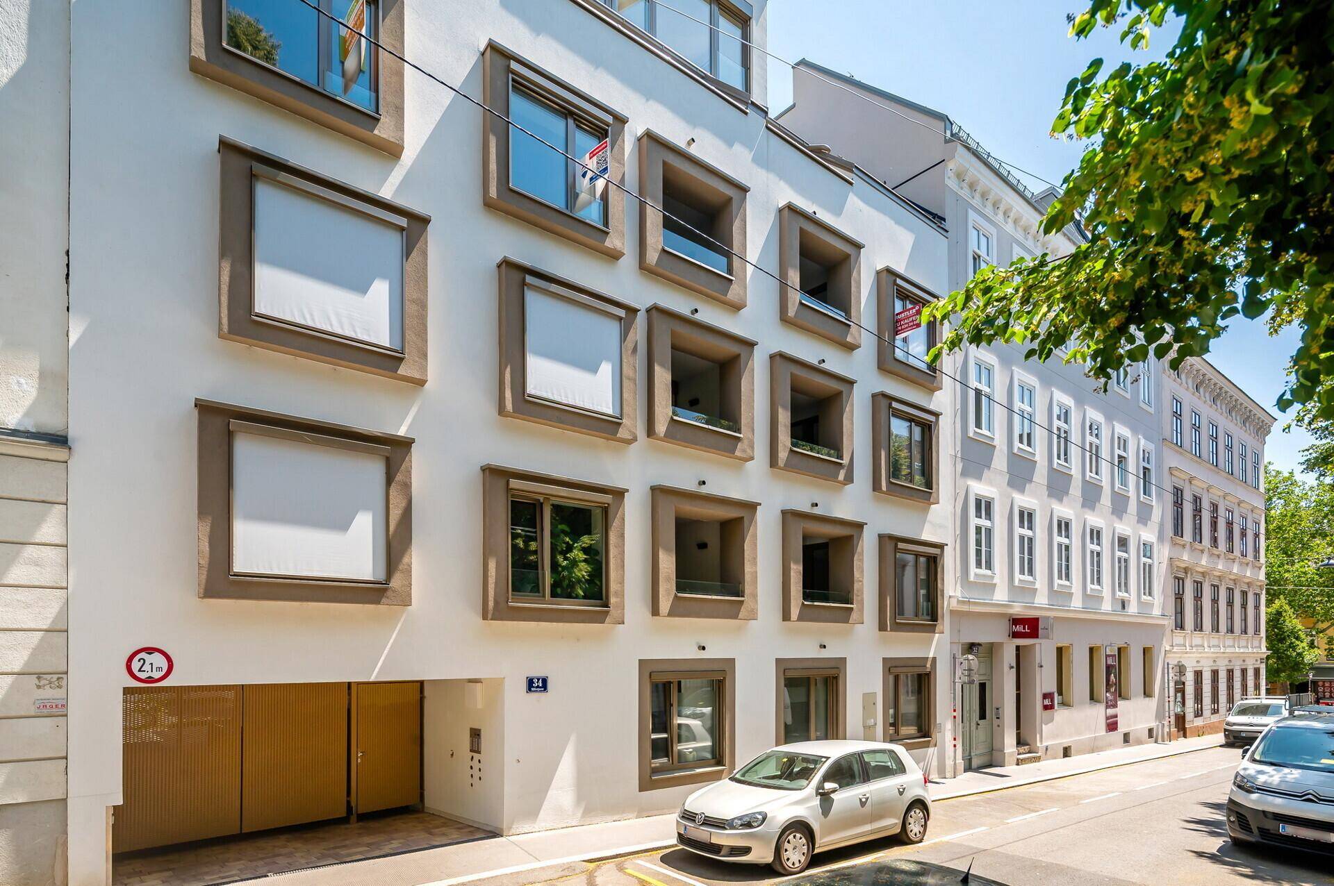 Moderne Gebäudefassade mit markanten Fenstern und Tiefgaragenzufahrt an einer belebten Stadtstraße.