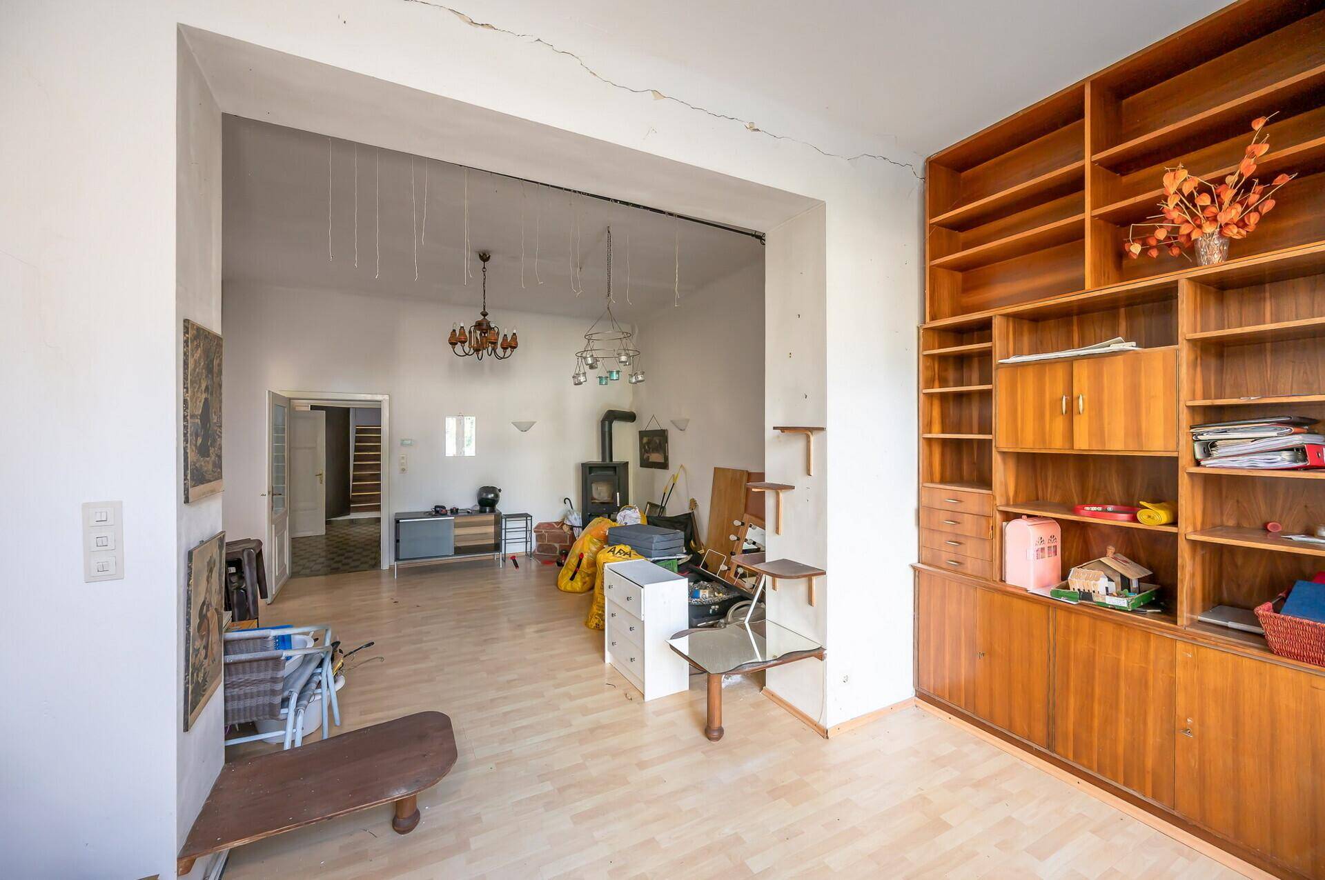 Wohnzimmer mit Parkettboden und Durchgang zu einem weiteren Raum, ausgestattet mit Holzregal.