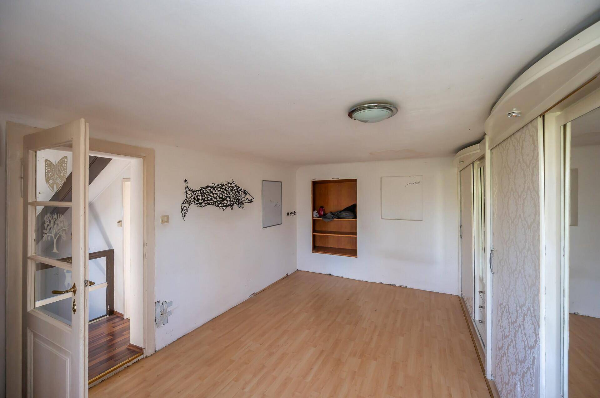 Geräumiges Zimmer mit Laminatboden und Einbauschränken, renovierungsbedürftig.