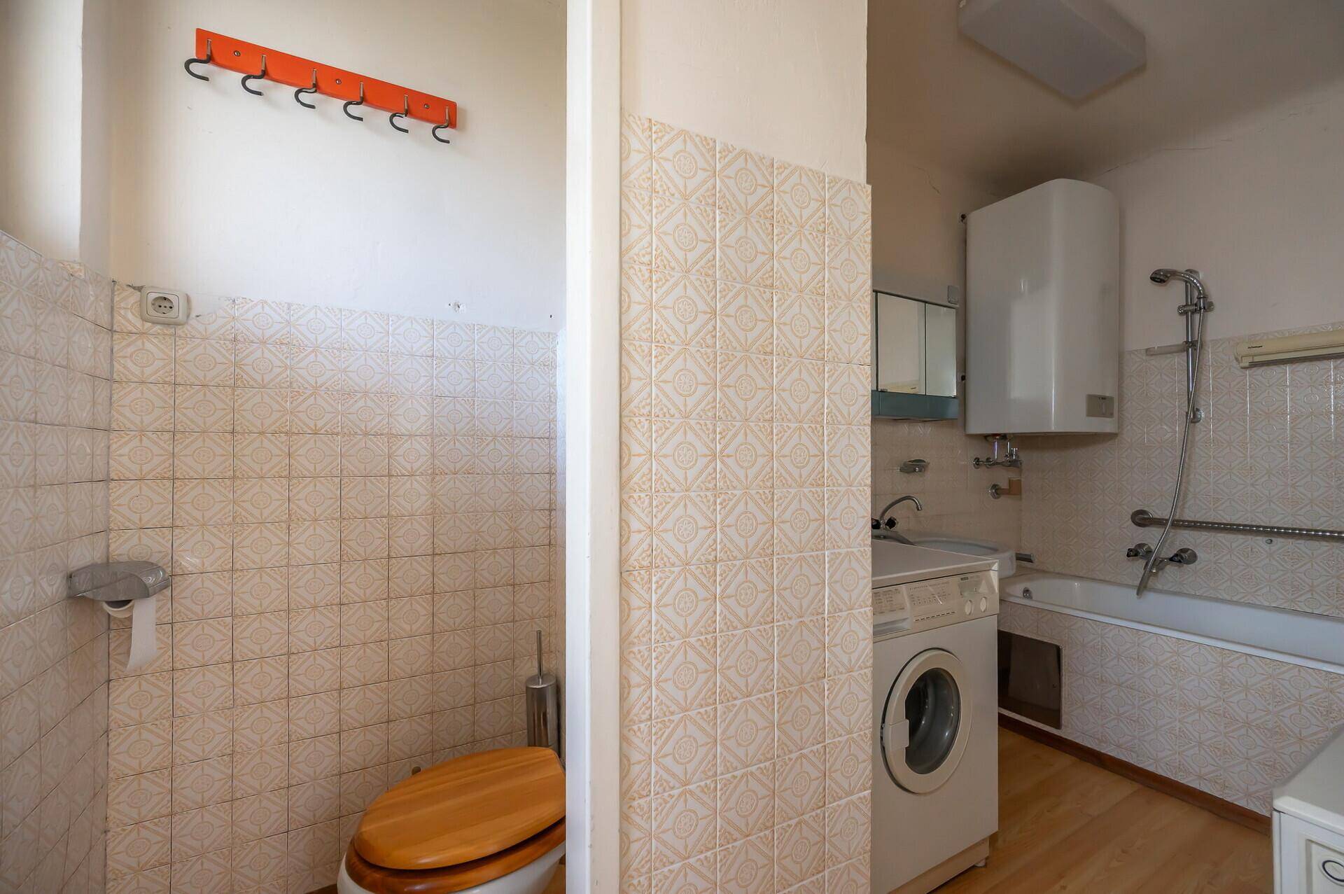 Badezimmer mit Toilette, Waschmaschine und Badewanne, mit älteren Fliesen, renovierungsbedürftig.