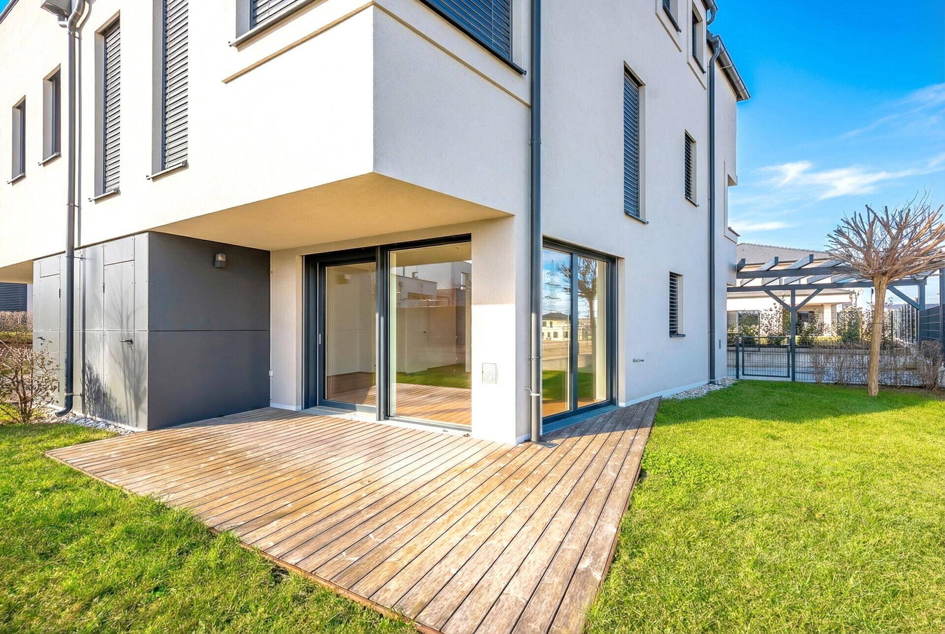 Moderne Hausfassade mit Holzterrasse und direktem Zugang zum Garten.