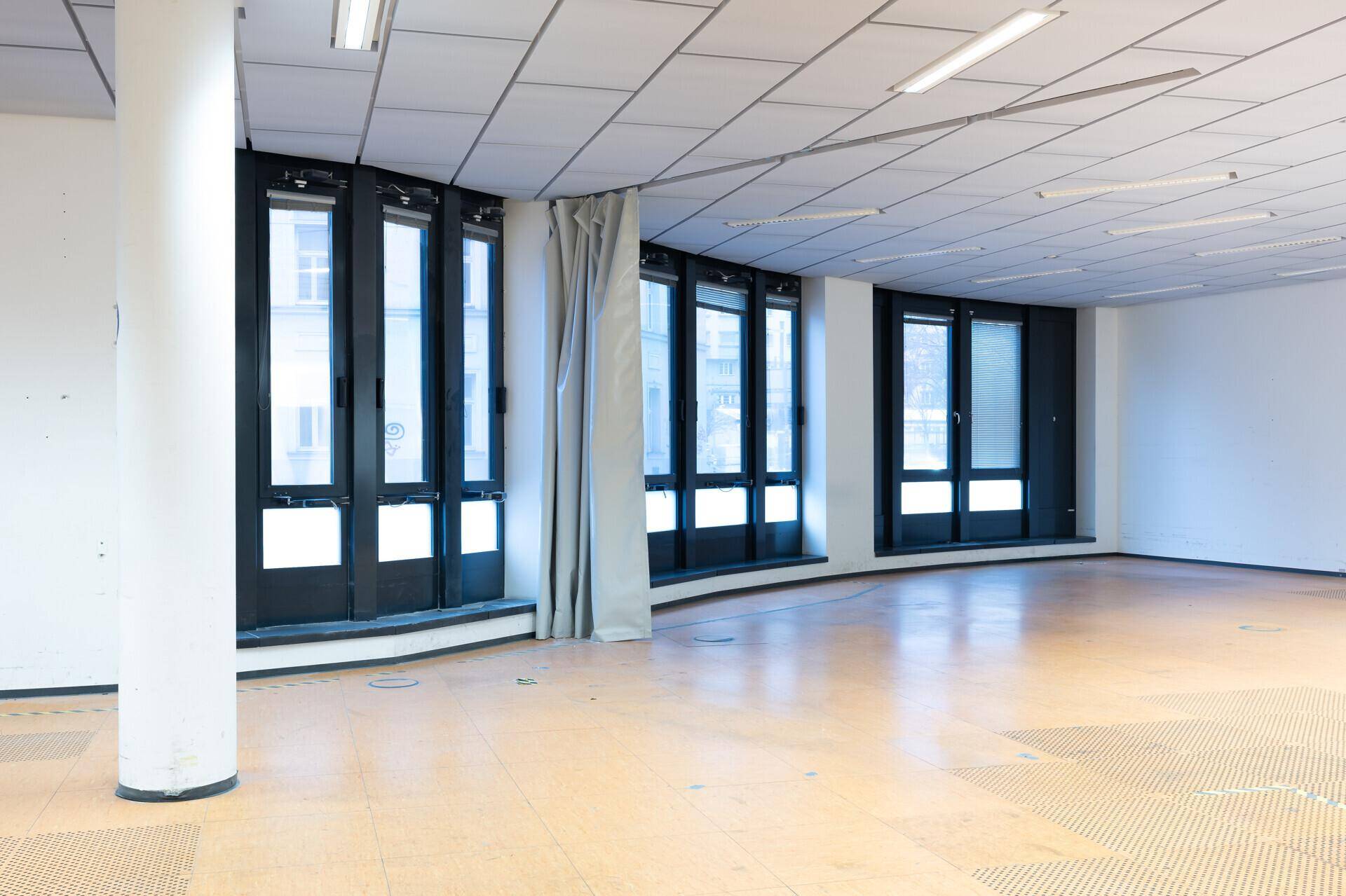 Geräumiger, leerer Gewerberaum mit geschwungener Fensterfront, hohen Decken und einem zentralen Pfeiler.
