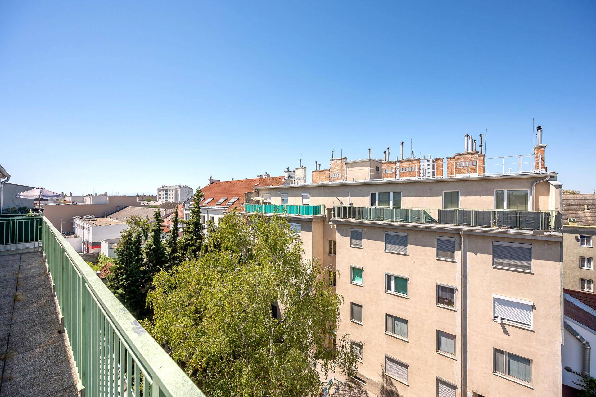 Blick vom Balkon auf die Dächer der Stadt und grüne Bäume.