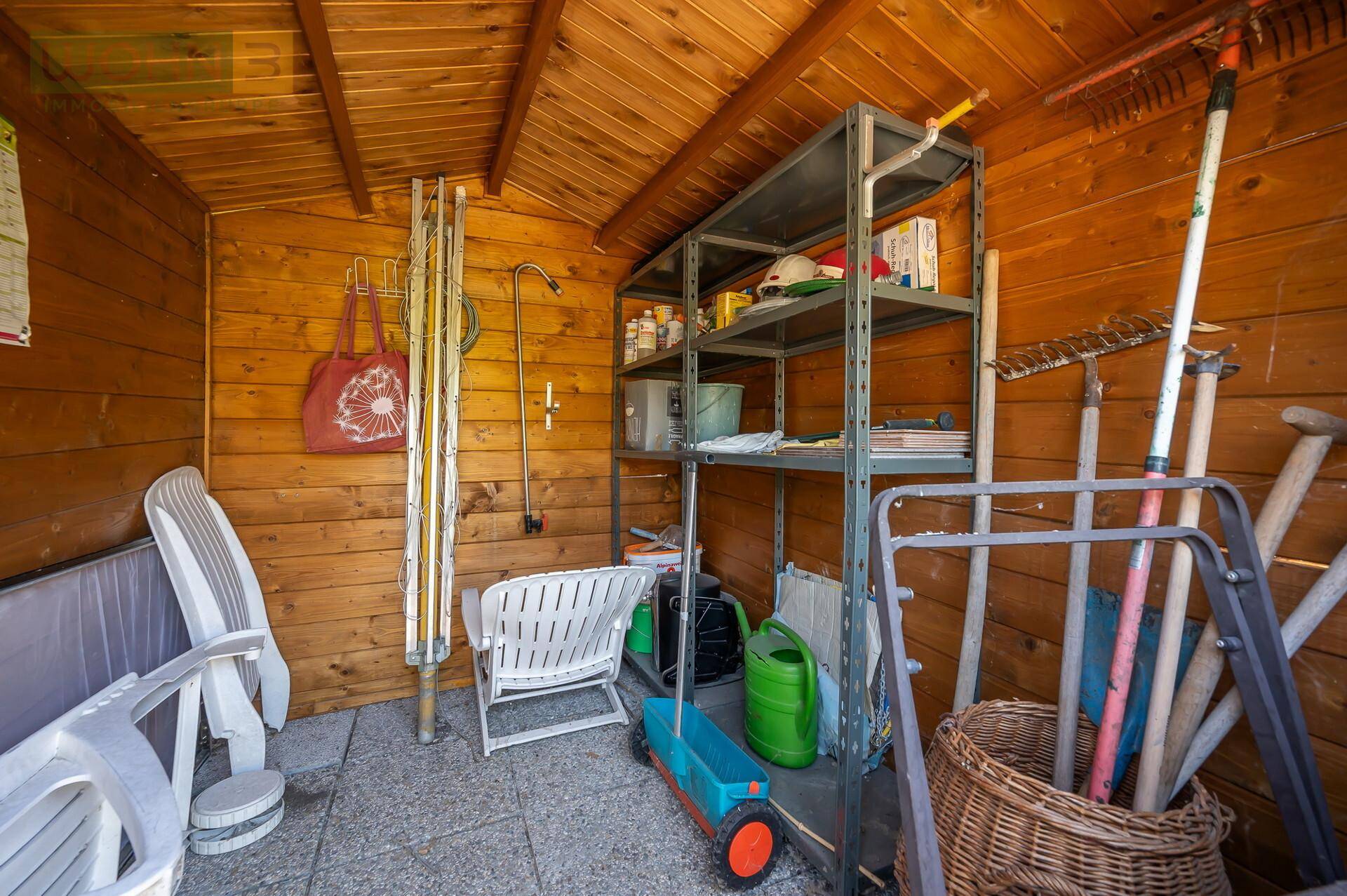 Innenansicht eines Holzgartenschuppens, gefüllt mit Gartengeräten und Gartenmöbeln.
