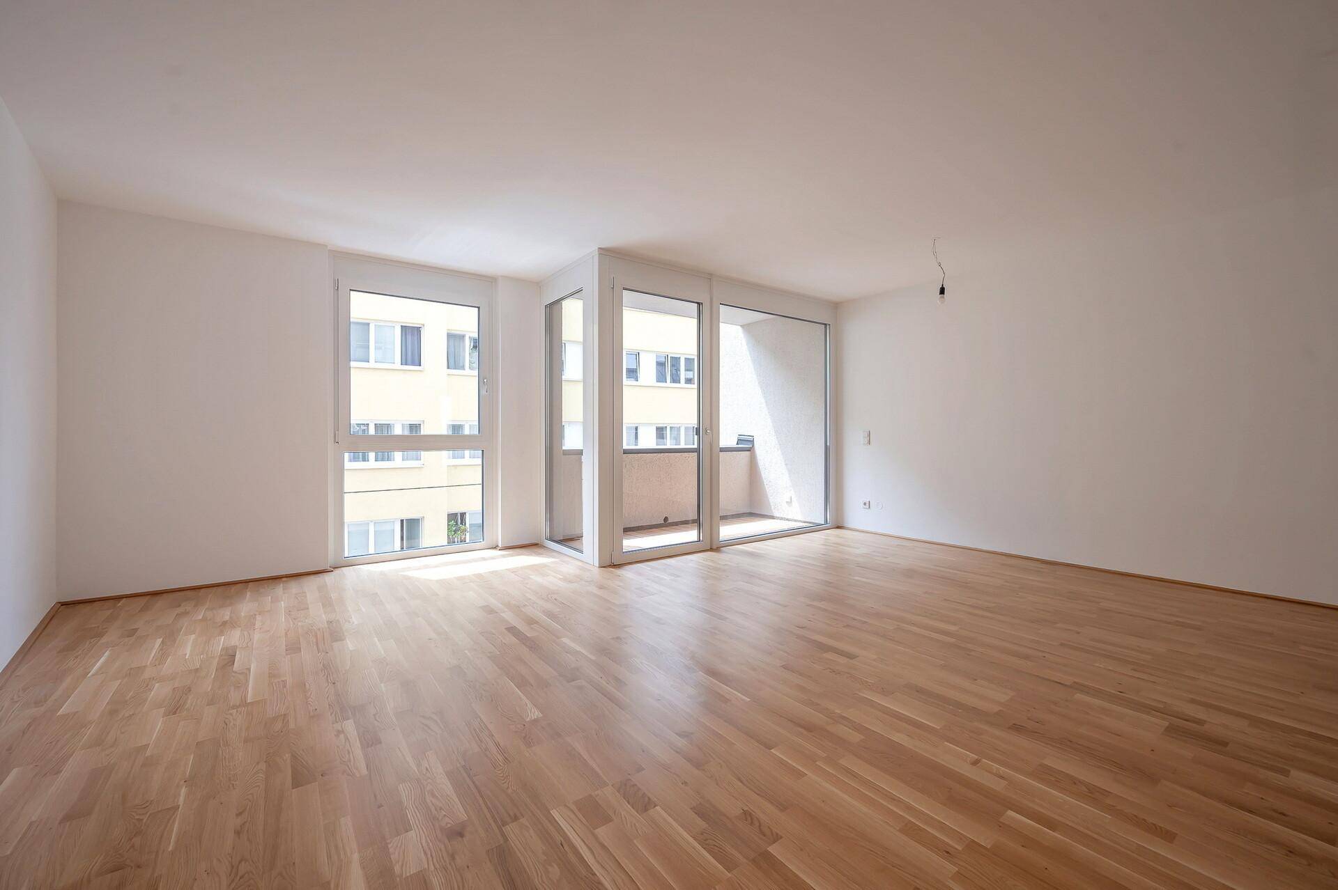 Geräumiger, heller Raum mit großen Fenstern und Holzboden, ideal für Wohn- oder Schlafbereich.