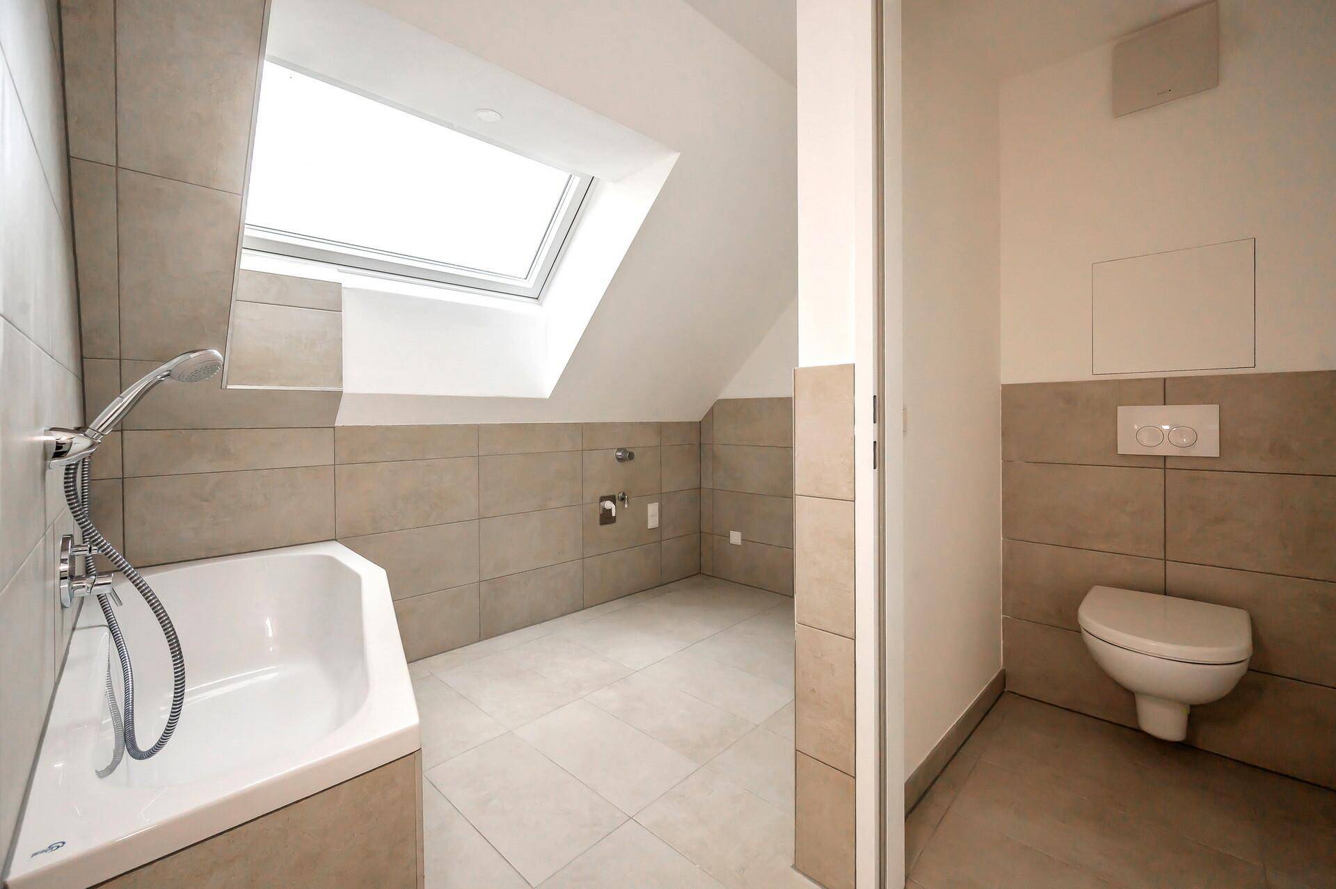 Modernes Badezimmer mit hellen Fliesen, Eckbadewanne, wandhängendem WC und Dachfenster.