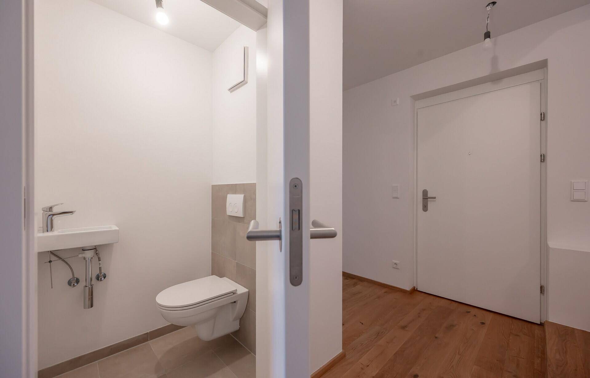 Modernes Gäste-WC mit Wand-WC, kleinem Waschbecken und hellen Fliesen.