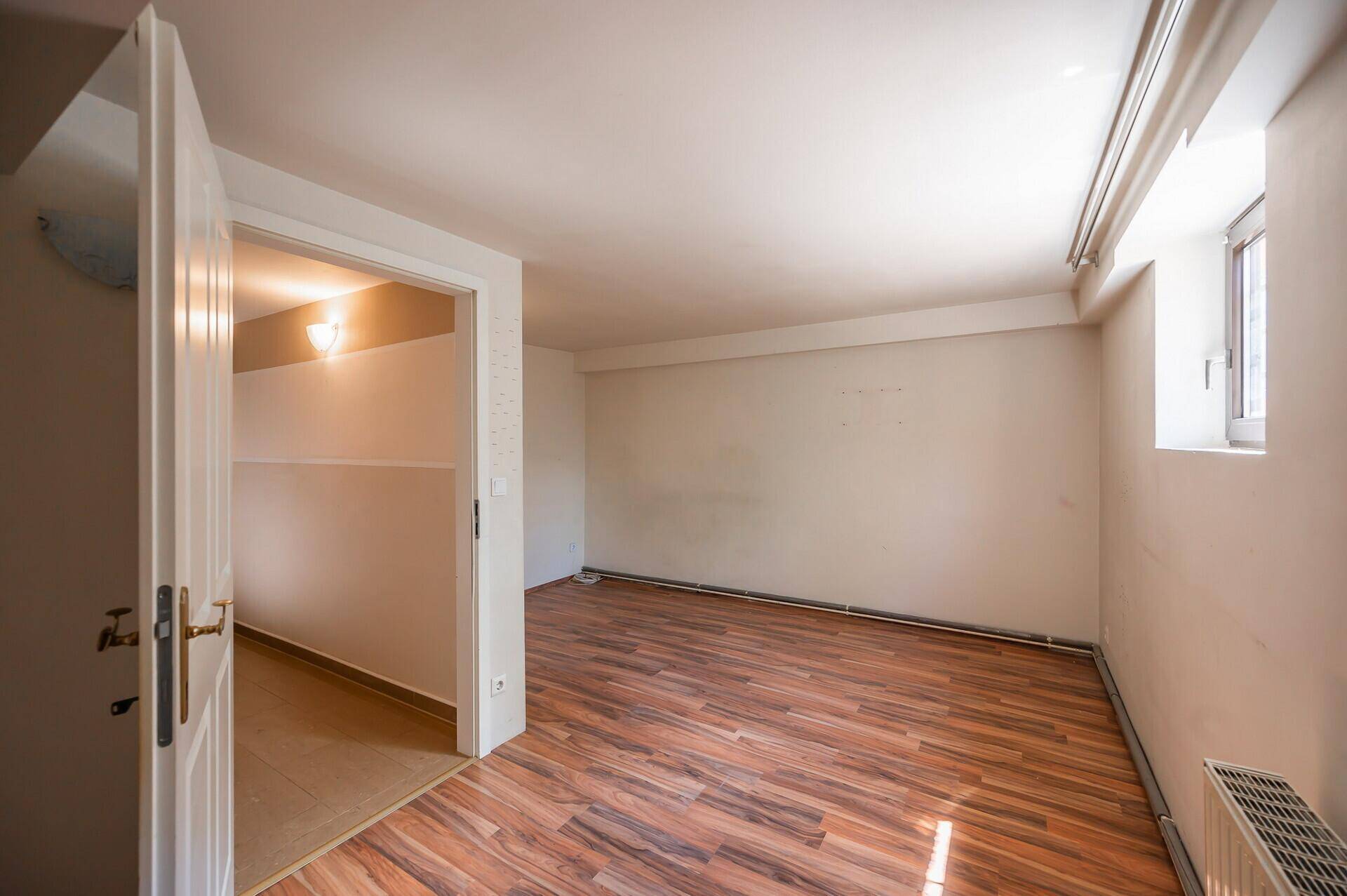 Helles Zimmer im Untergeschoss mit Holzoptikboden und kleinem Fenster.