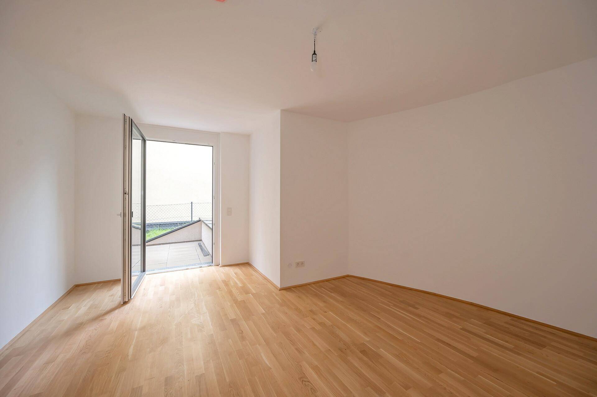 Helles, leeres Zimmer mit Holzboden und Zugang zu einem Außenbereich, ideal für individuelle Gestaltung.