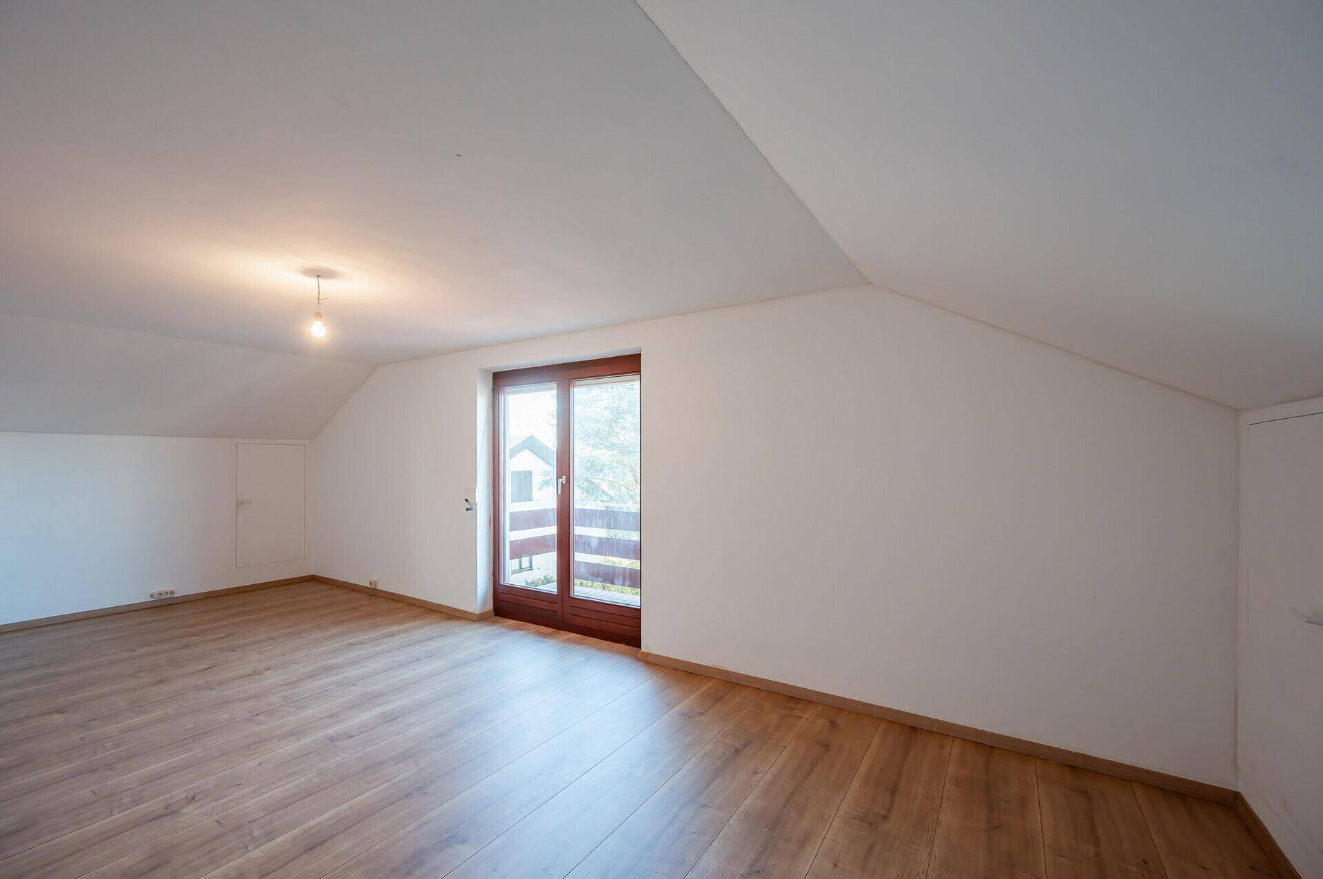 Helles Zimmer im Dachgeschoss mit Schrägen, Laminatboden und Zugang zu einem Balkon.
