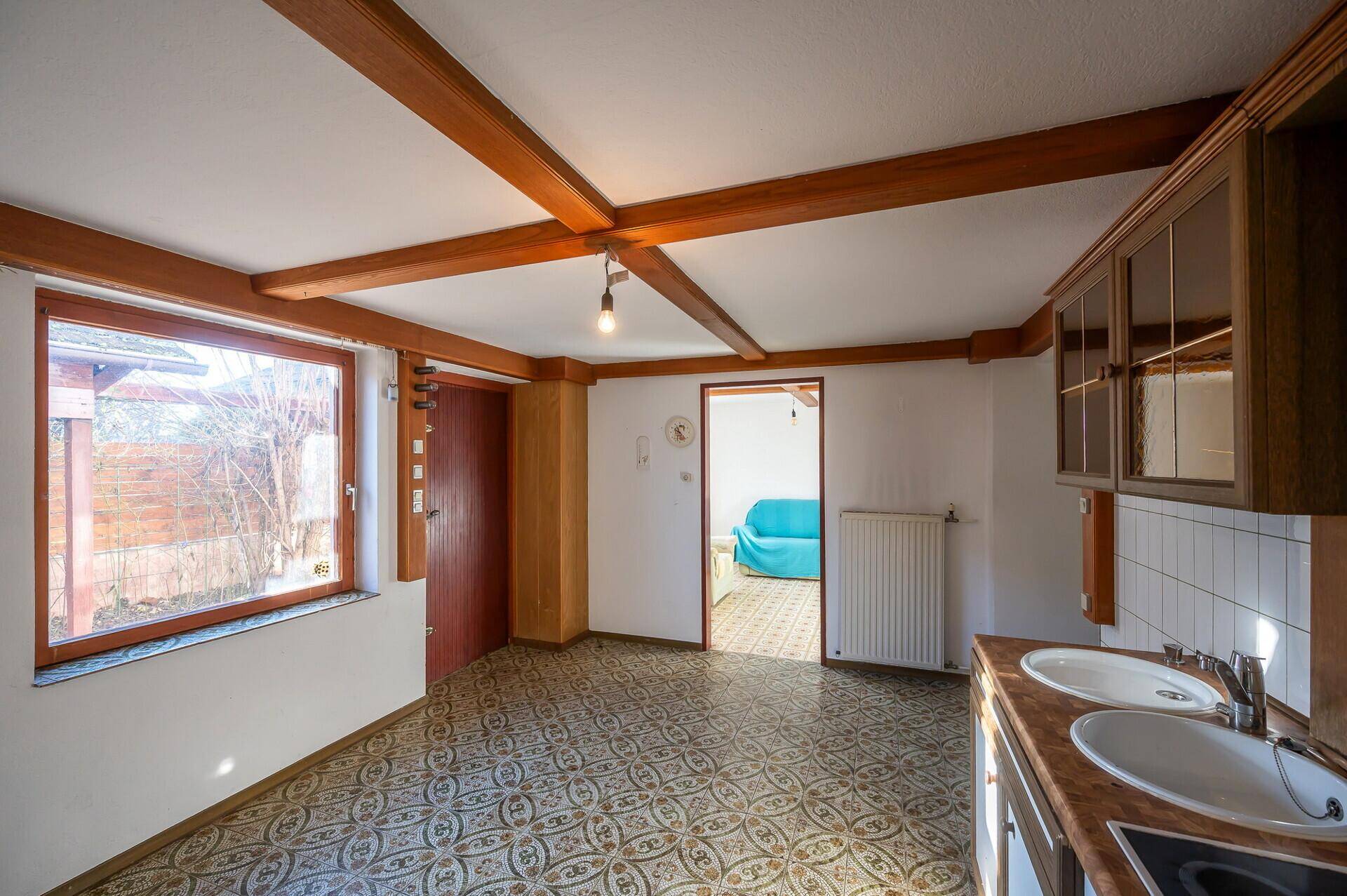 Helle Wohnküche mit Holzbalken, Einbauschränken und Fensterblick in den Garten.
