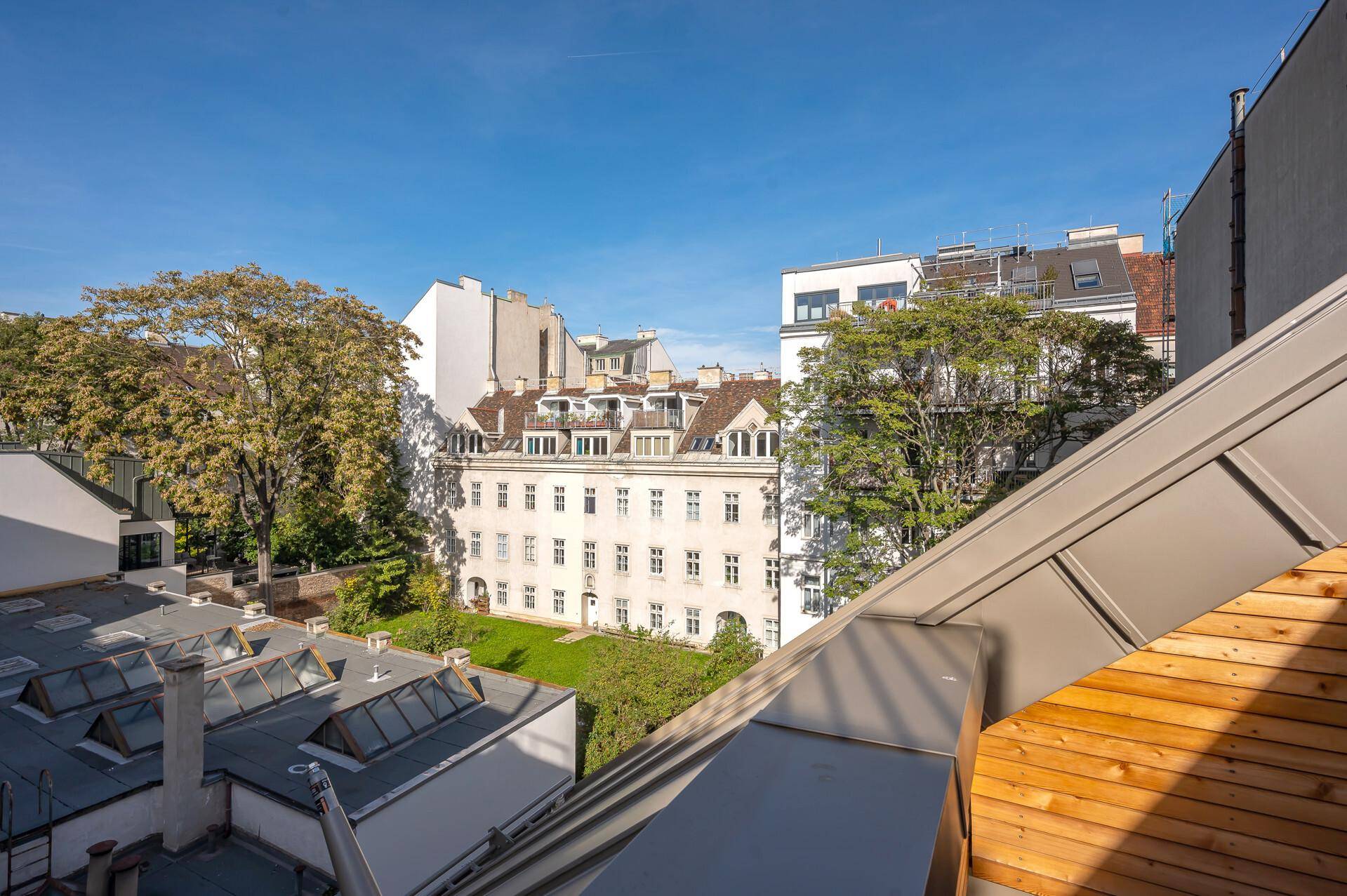 Panoramablick über die Dächer der Stadt mit grünen Innenhöfen und umliegenden Gebäuden unter blauem Himmel.
