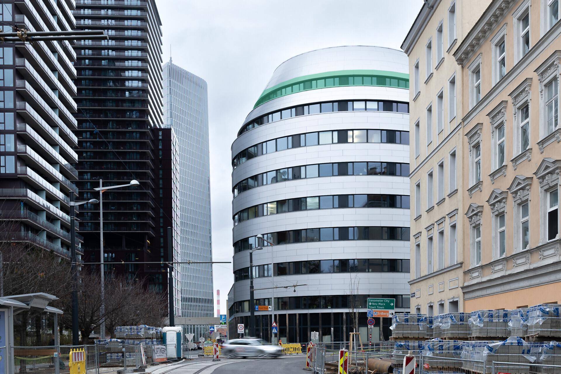 Moderne Architektur mit geschwungenem Gebäude und hohen Türmen in einer städtischen Umgebung.