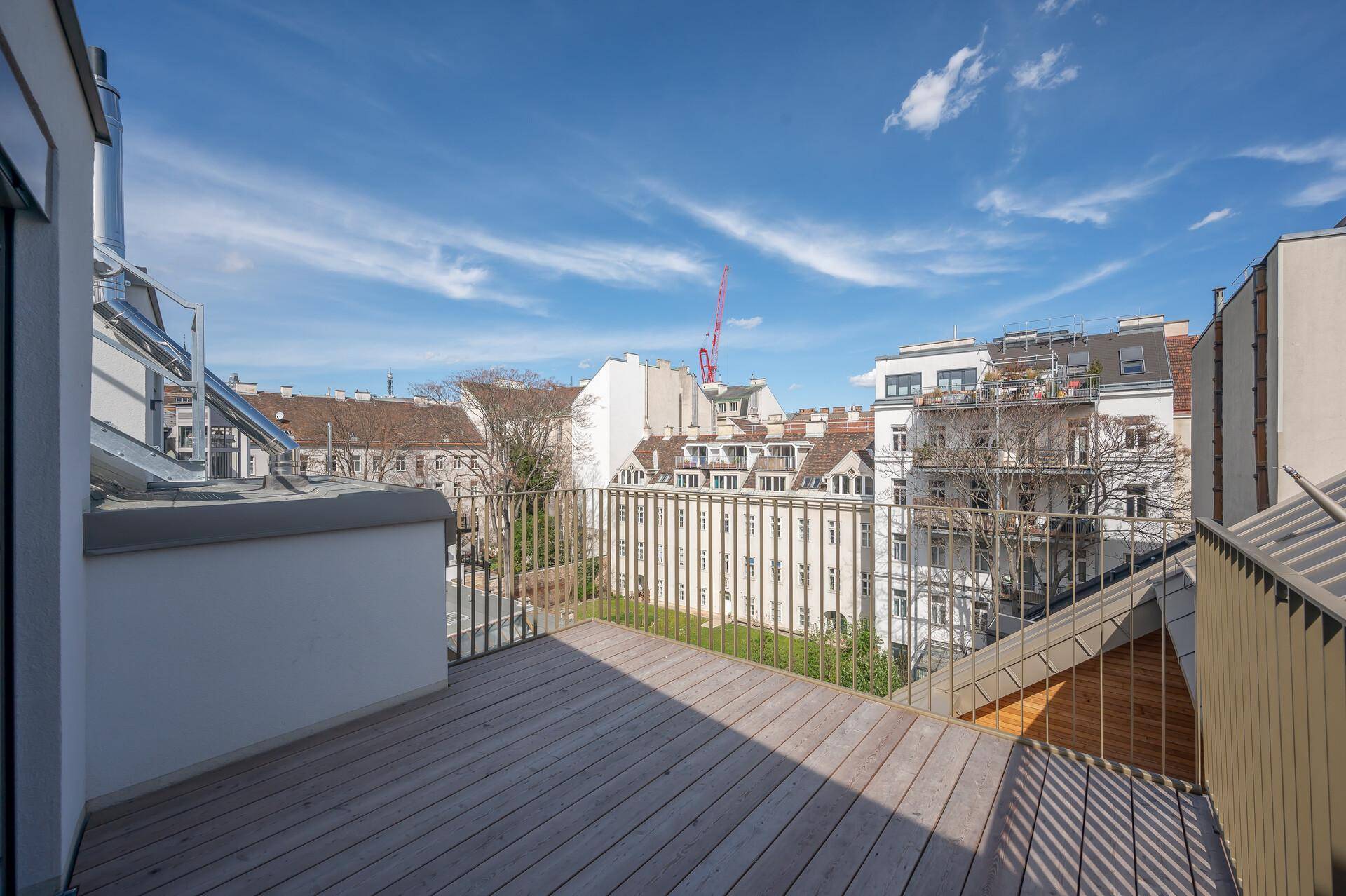 Geräumige Holzterrasse mit Metallgeländer und weitem Blick über die umliegenden Gebäude der Stadt.