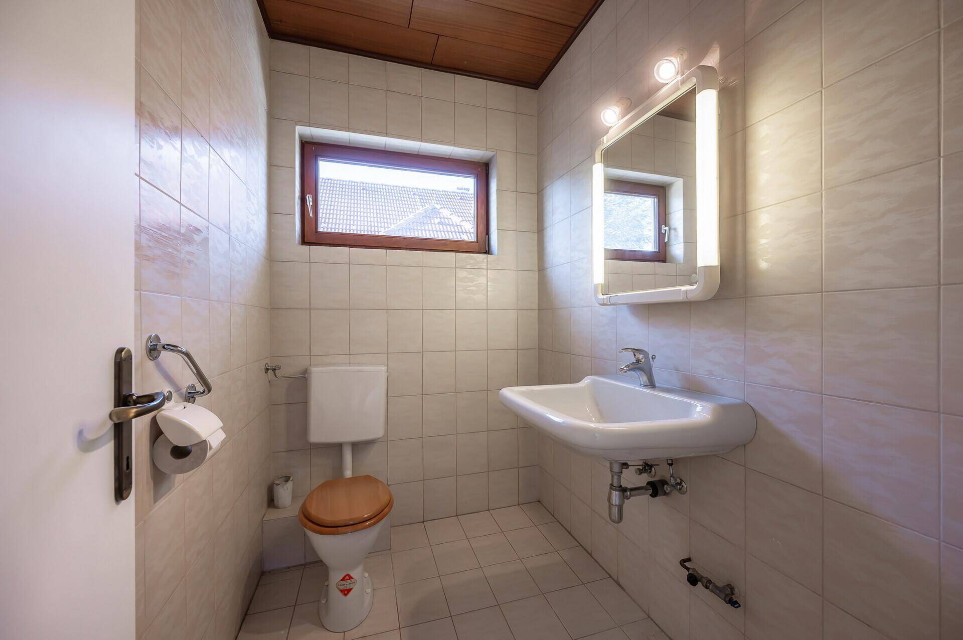 Gäste-WC mit Toilette, Waschbecken, Spiegel und vollständig gefliesten Wänden.