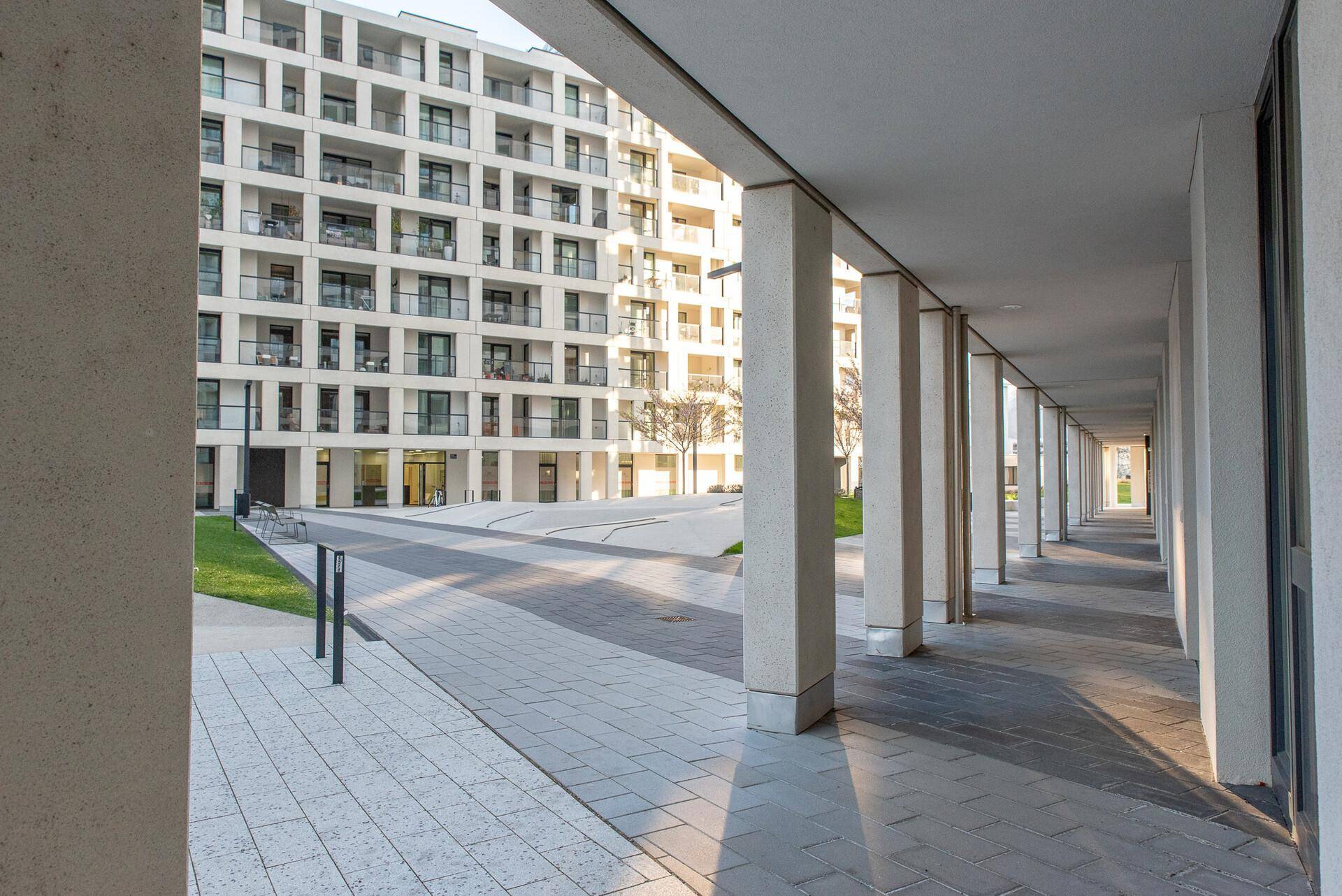 Überdachter Gehweg mit Säulen vor einer modernen Wohnanlage mit vielen Balkonen.
