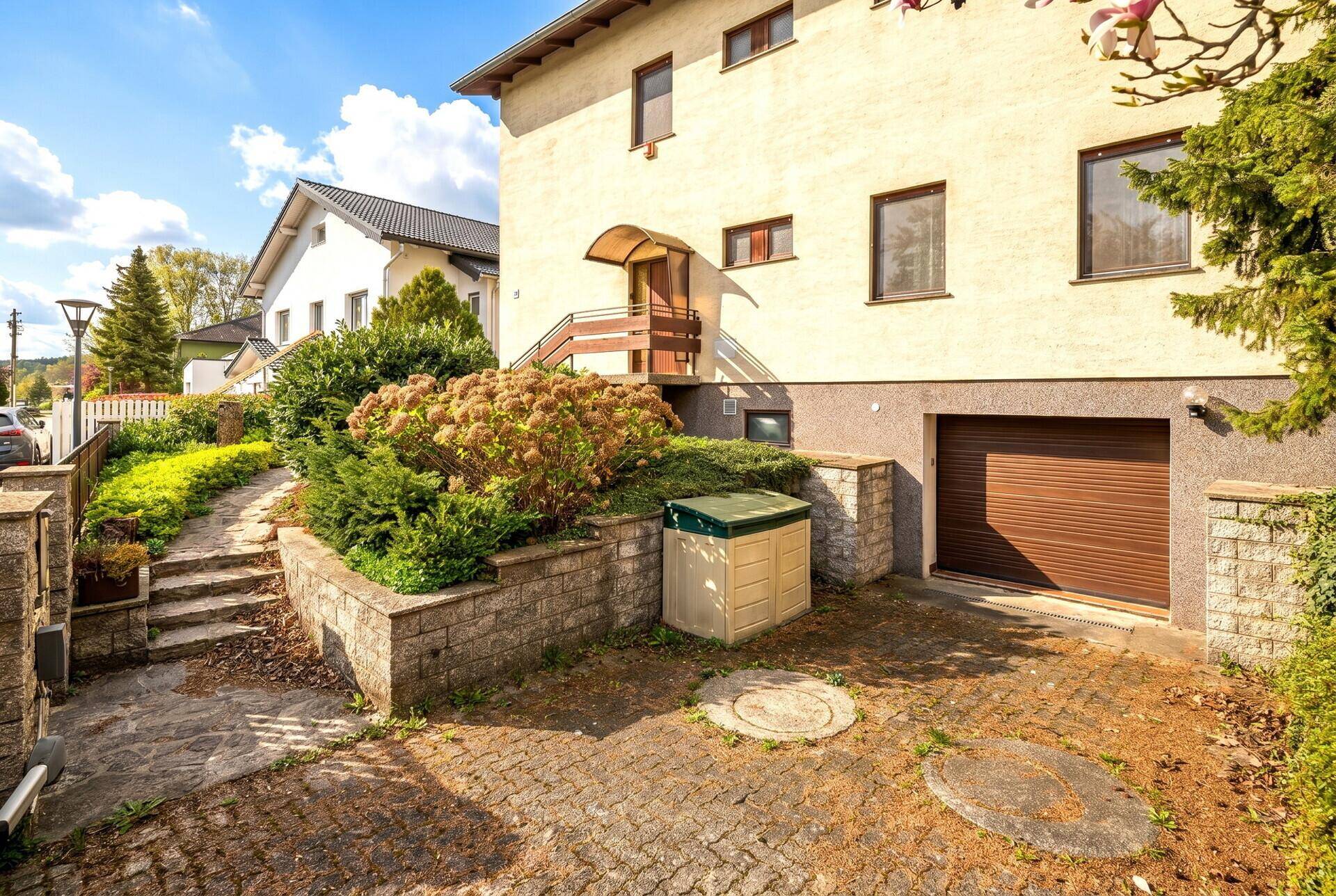 Seitenansicht des Hauses mit Garagentor, Eingangsbereich und einer gepflasterten Auffahrt.