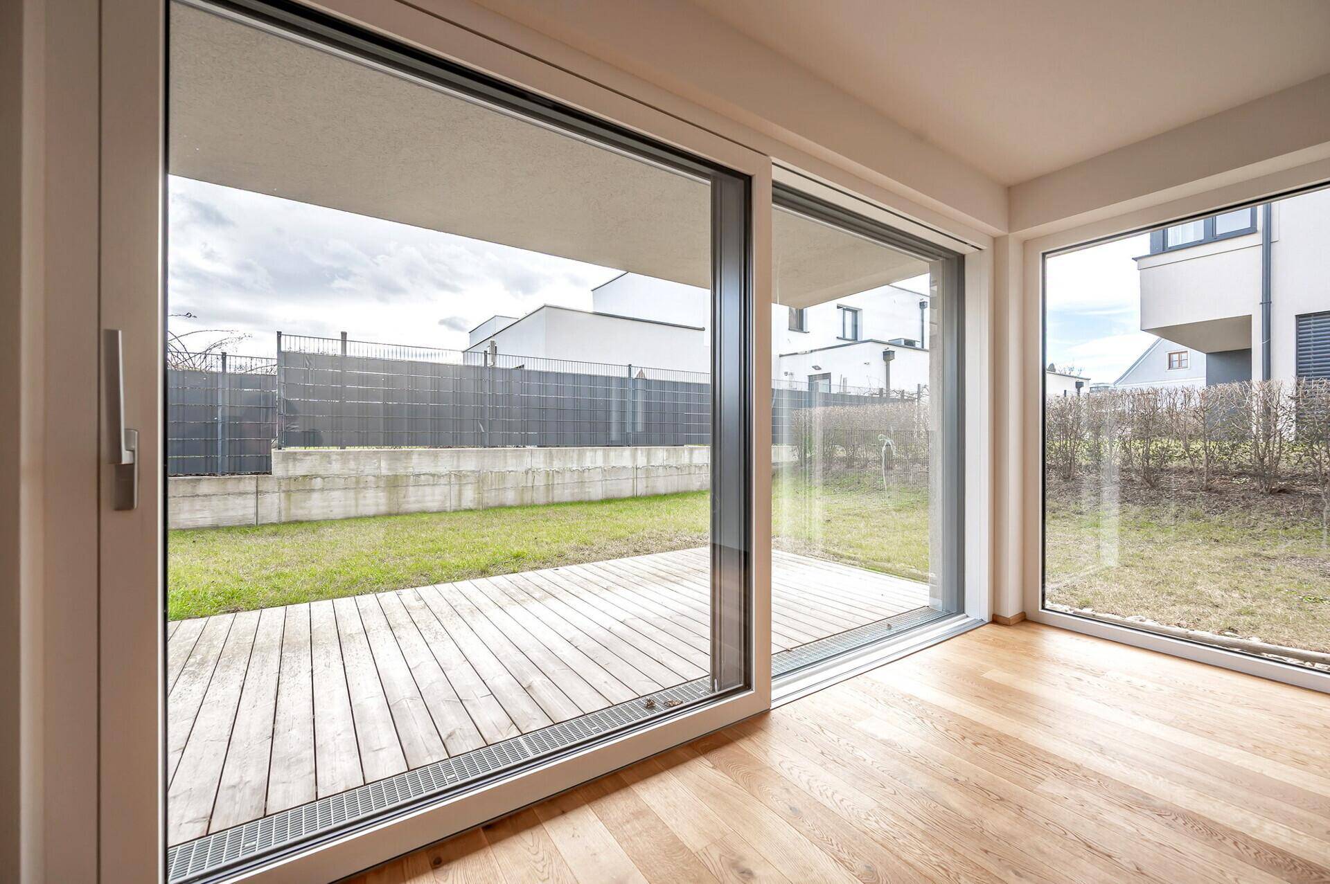Große Fensterfront mit Blick auf die Holzterrasse und den Garten.