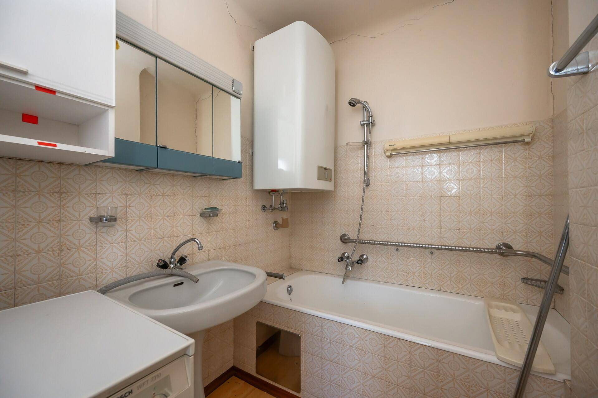 Badezimmer mit Badewanne, Waschbecken und Spiegelschrank, mit älteren Fliesen, renovierungsbedürftig.