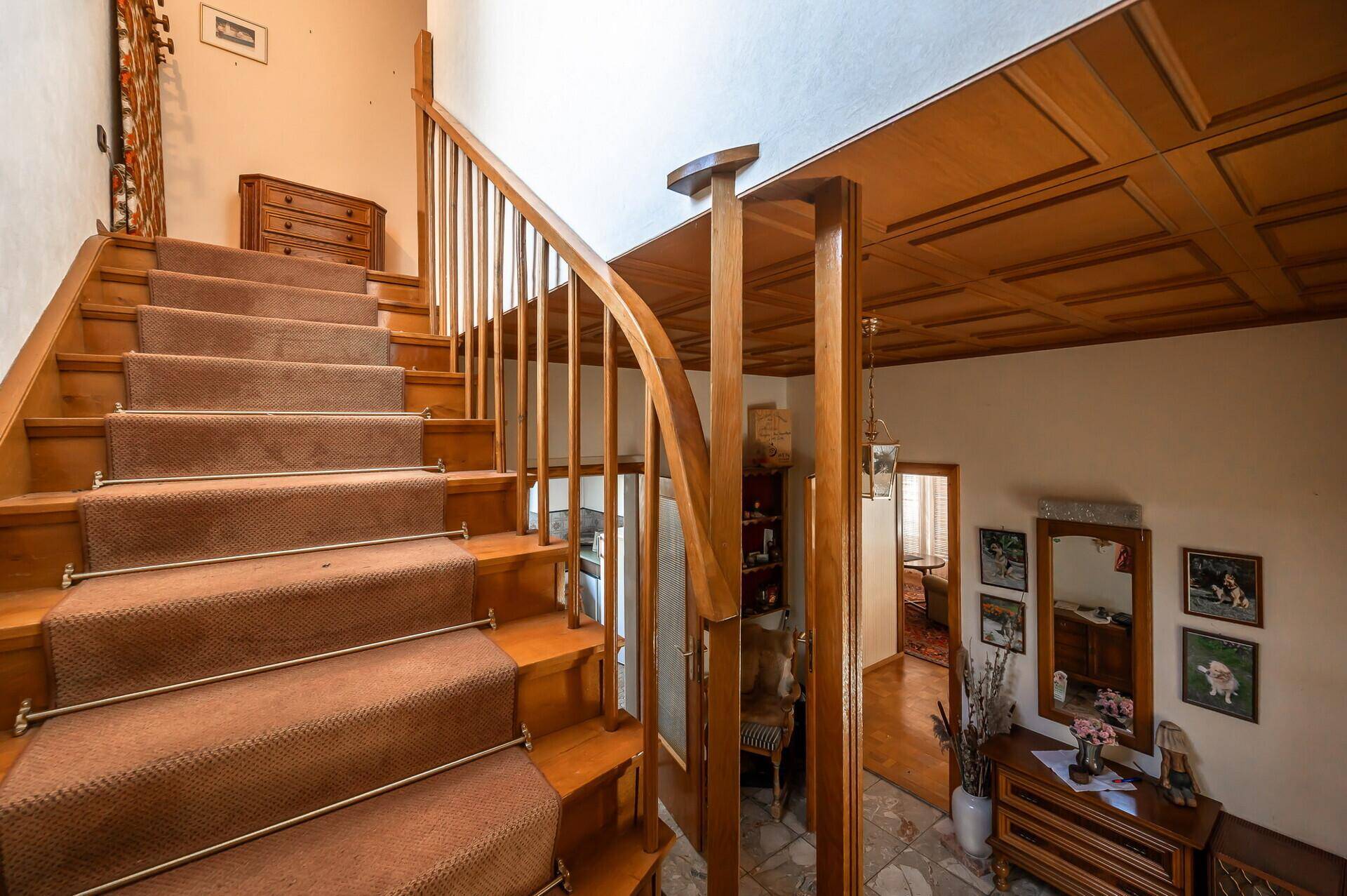 Elegante Holztreppe mit Teppichstufen und einer Kassettendecke, die in die obere Etage führt.