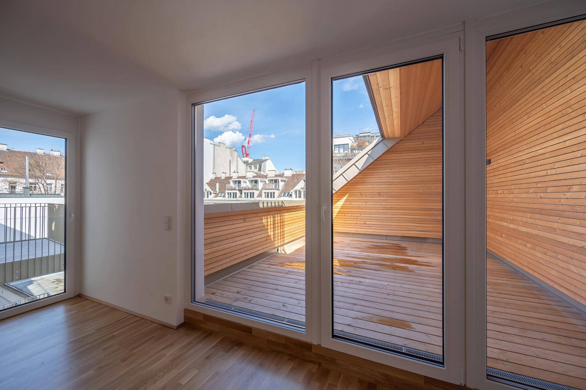Große Fensterfront mit Blick auf die Holzterrasse und die umliegenden Dächer der Stadt.