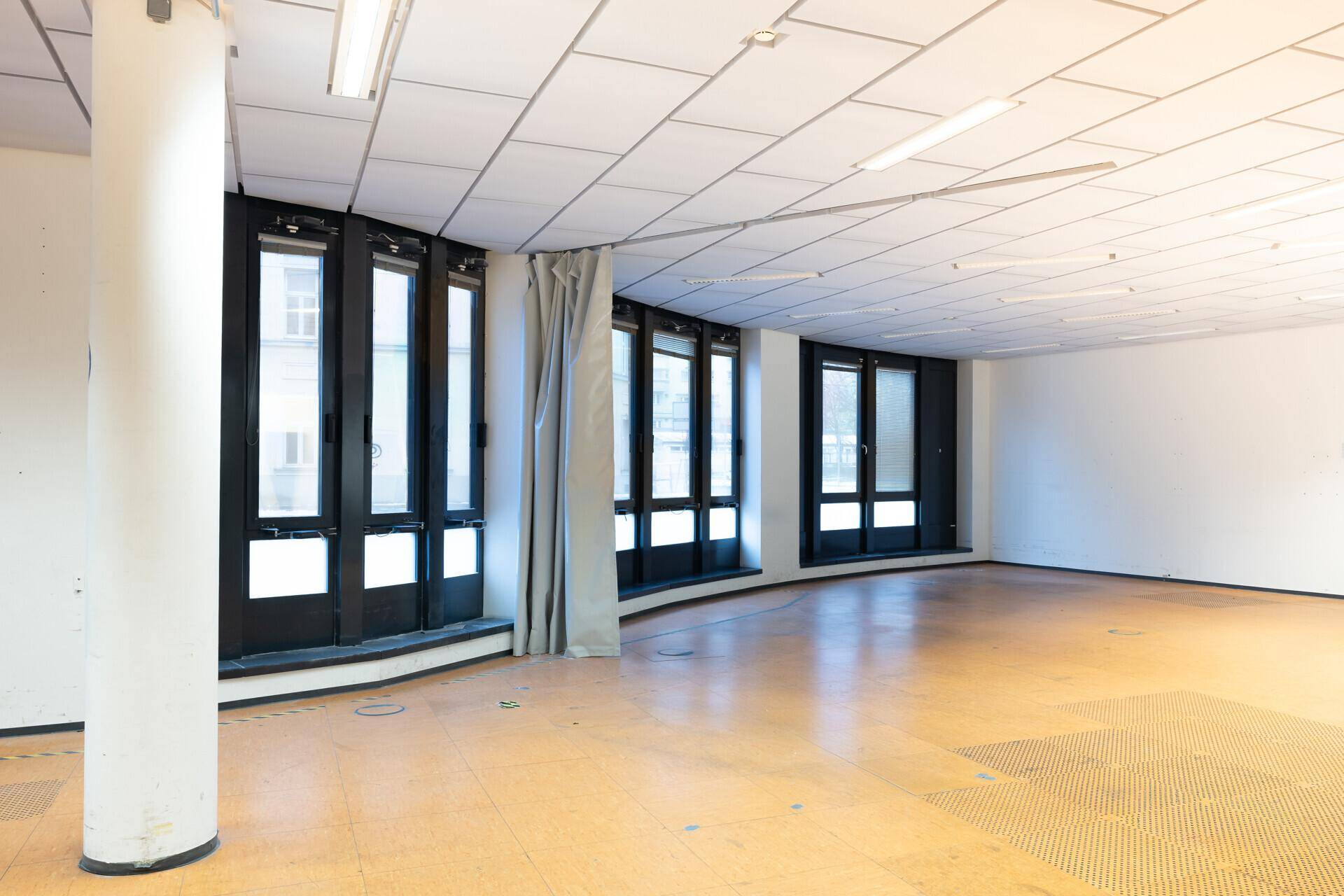 Heller Gewerberaum mit einer markanten, gebogenen Fensterfront und einem tragenden Säulenpfeiler.