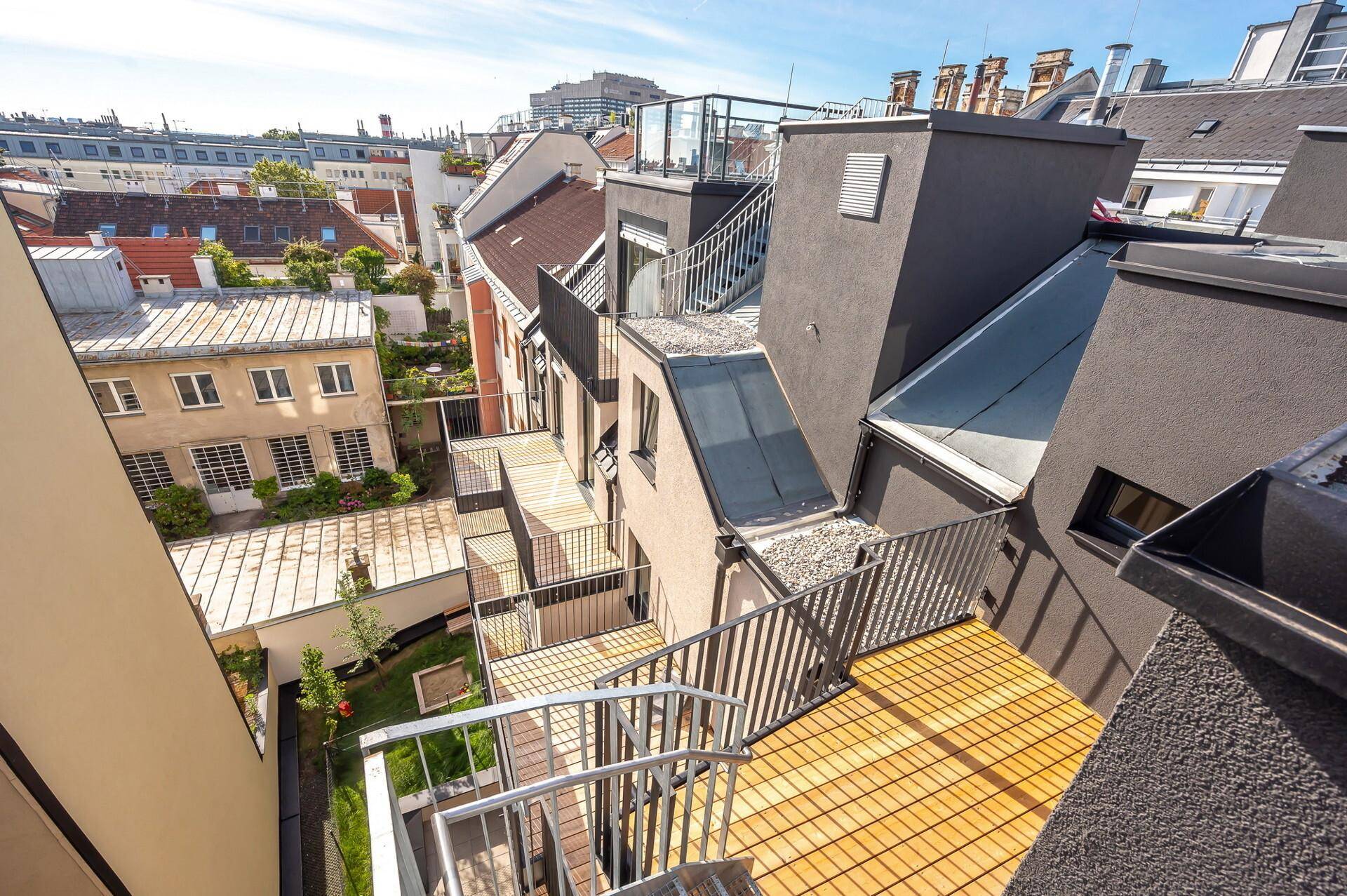 Dachlandschaft eines modernen Wohnkomplexes mit mehreren Terrassen und Stadtblick.