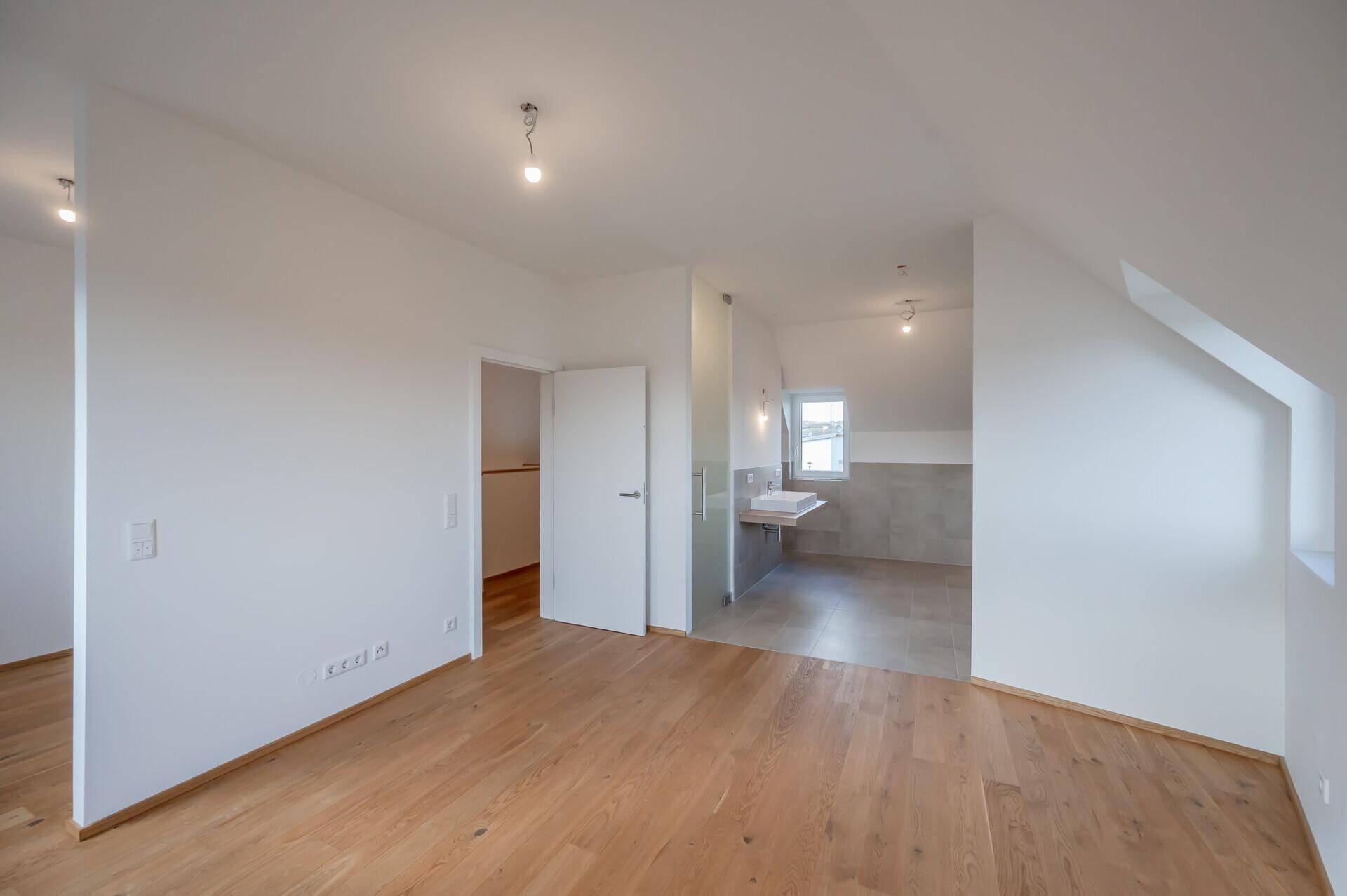 Schlafzimmer mit Eichenparkett und direktem Zugang zu einem modernen Badezimmer.
