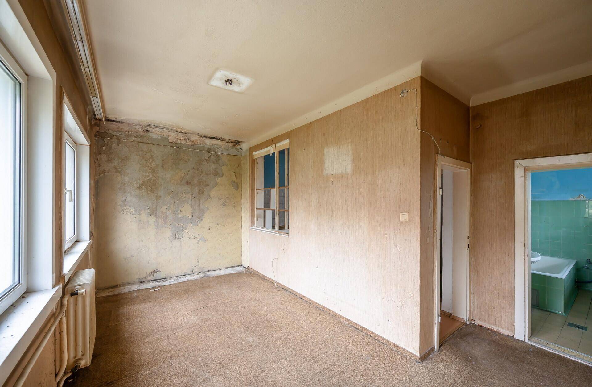Wohnraum mit Teppichboden und Zugang zu einem Badezimmer, bereit zur Sanierung.
