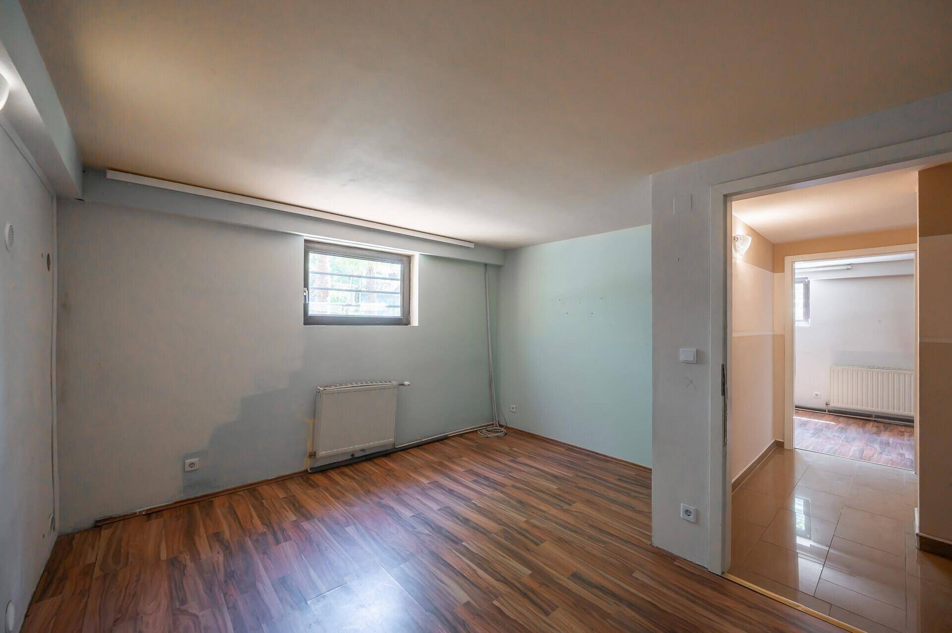 Geräumiger Kellerraum mit Laminatboden, kleinem Fenster und Zugang zu weiteren Räumen.