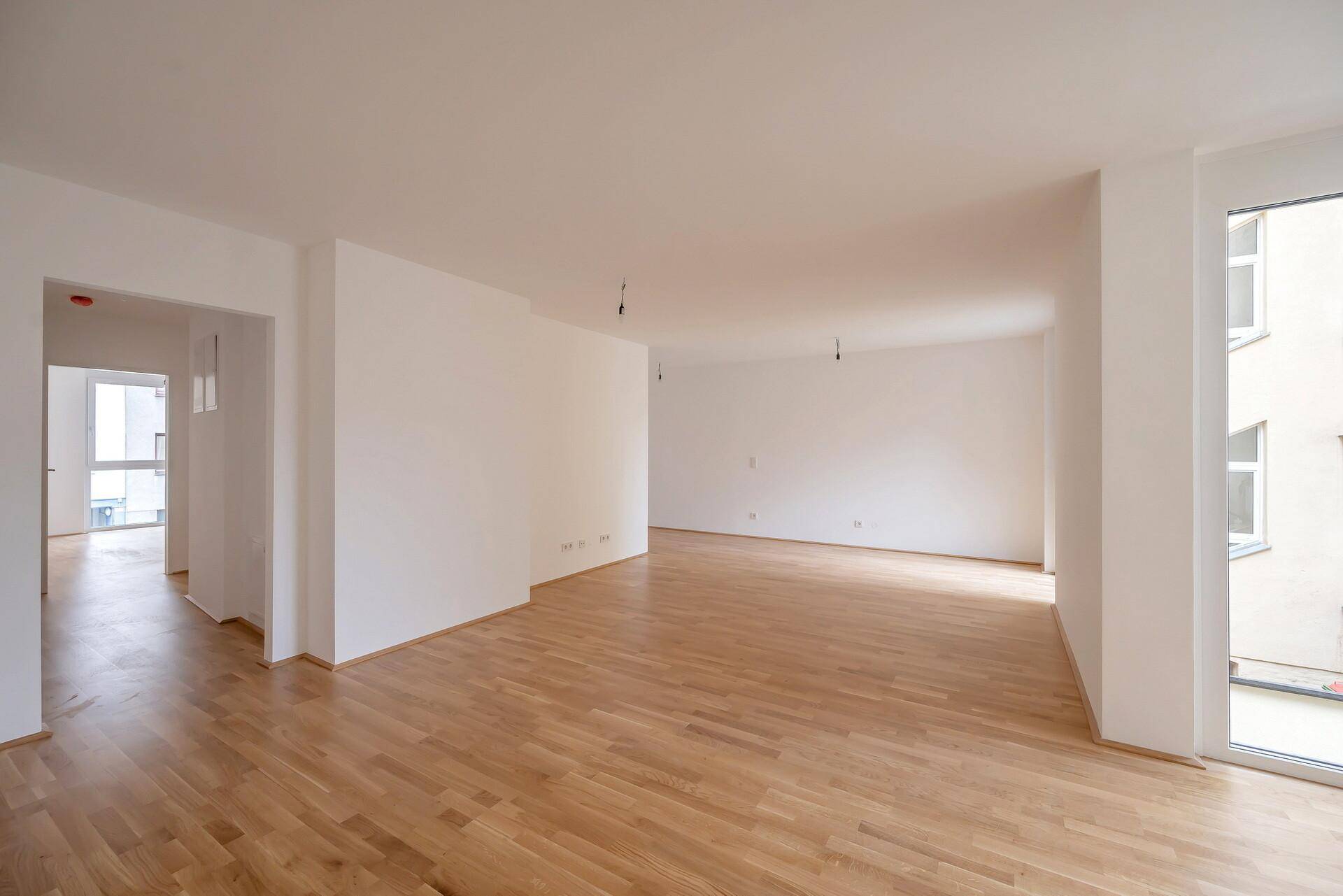 Großer, lichtdurchfluteter Wohnbereich mit hellem Parkettboden in einem Neubau.