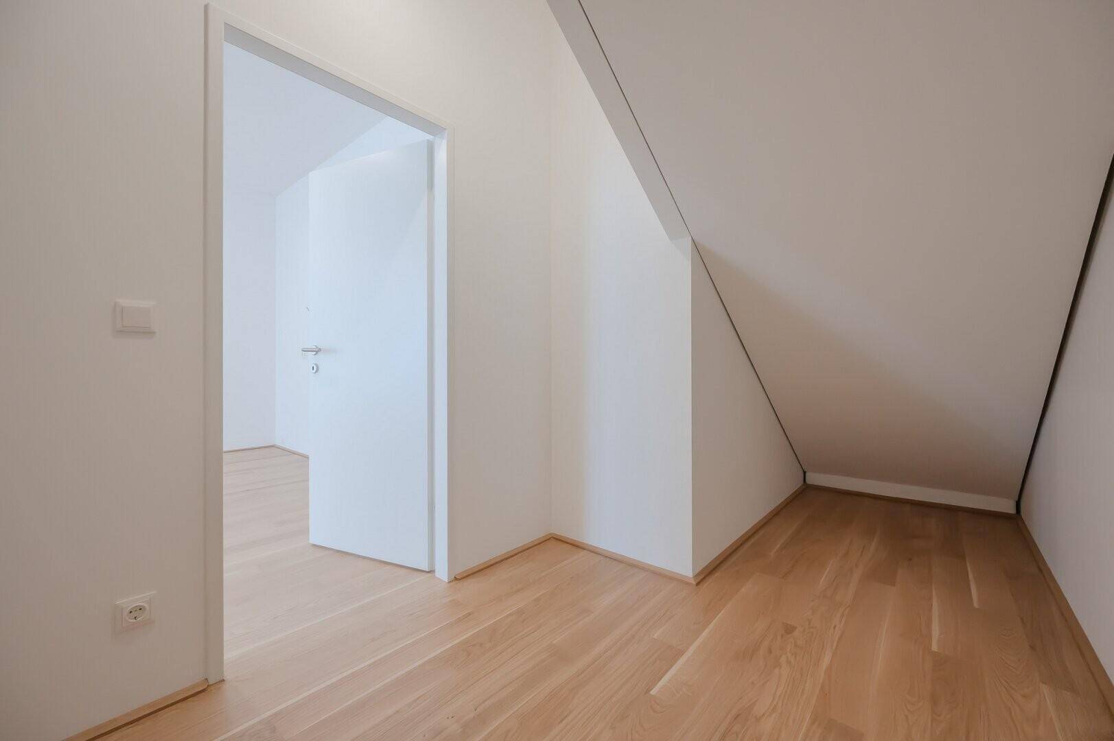 Heller Raum im Dachgeschoss mit schräger Decke und Holzboden.