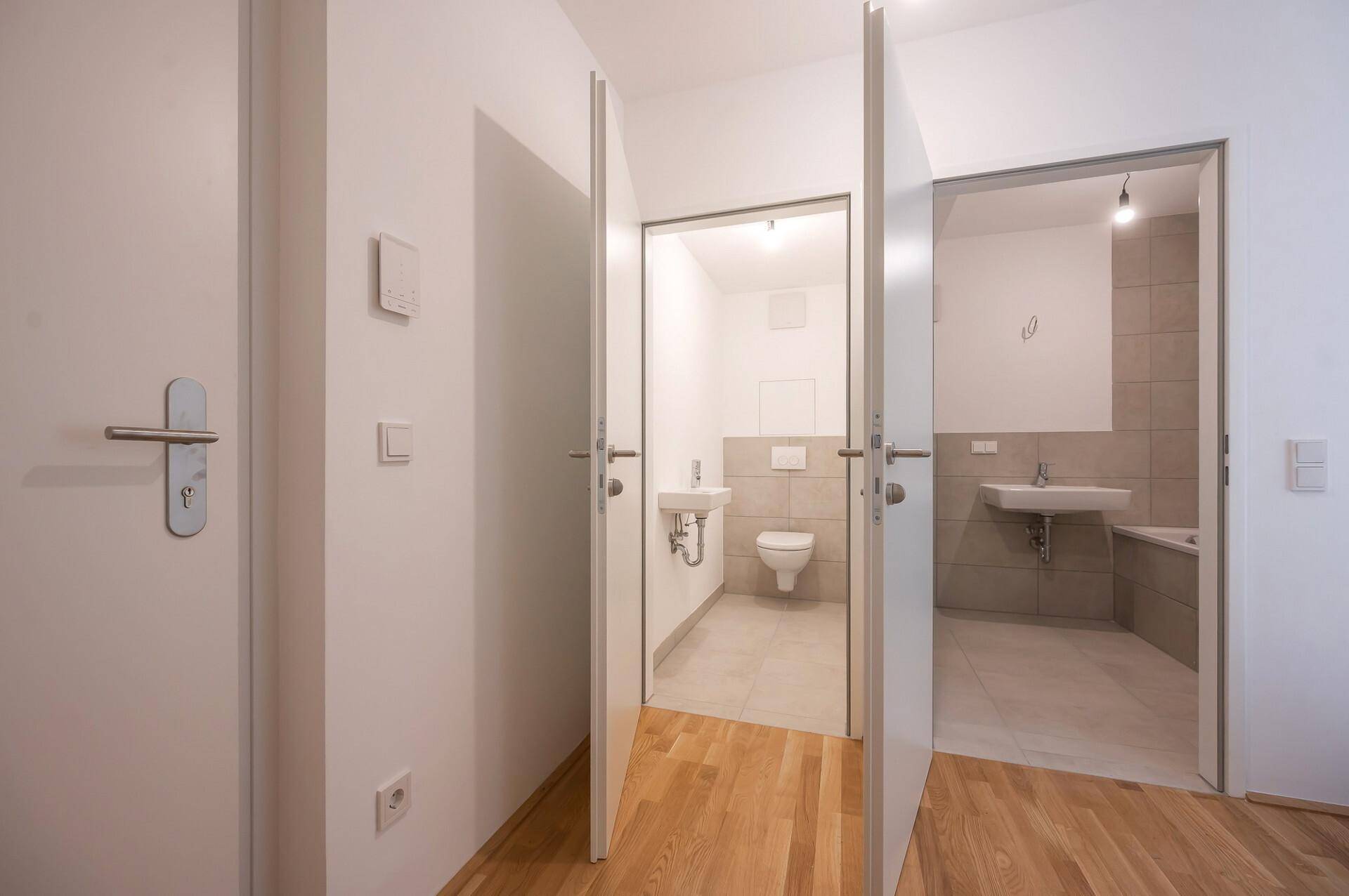 Flur mit Zugang zu einem Gäste-WC und einem Badezimmer, ausgestattet mit hellem Parkettboden.