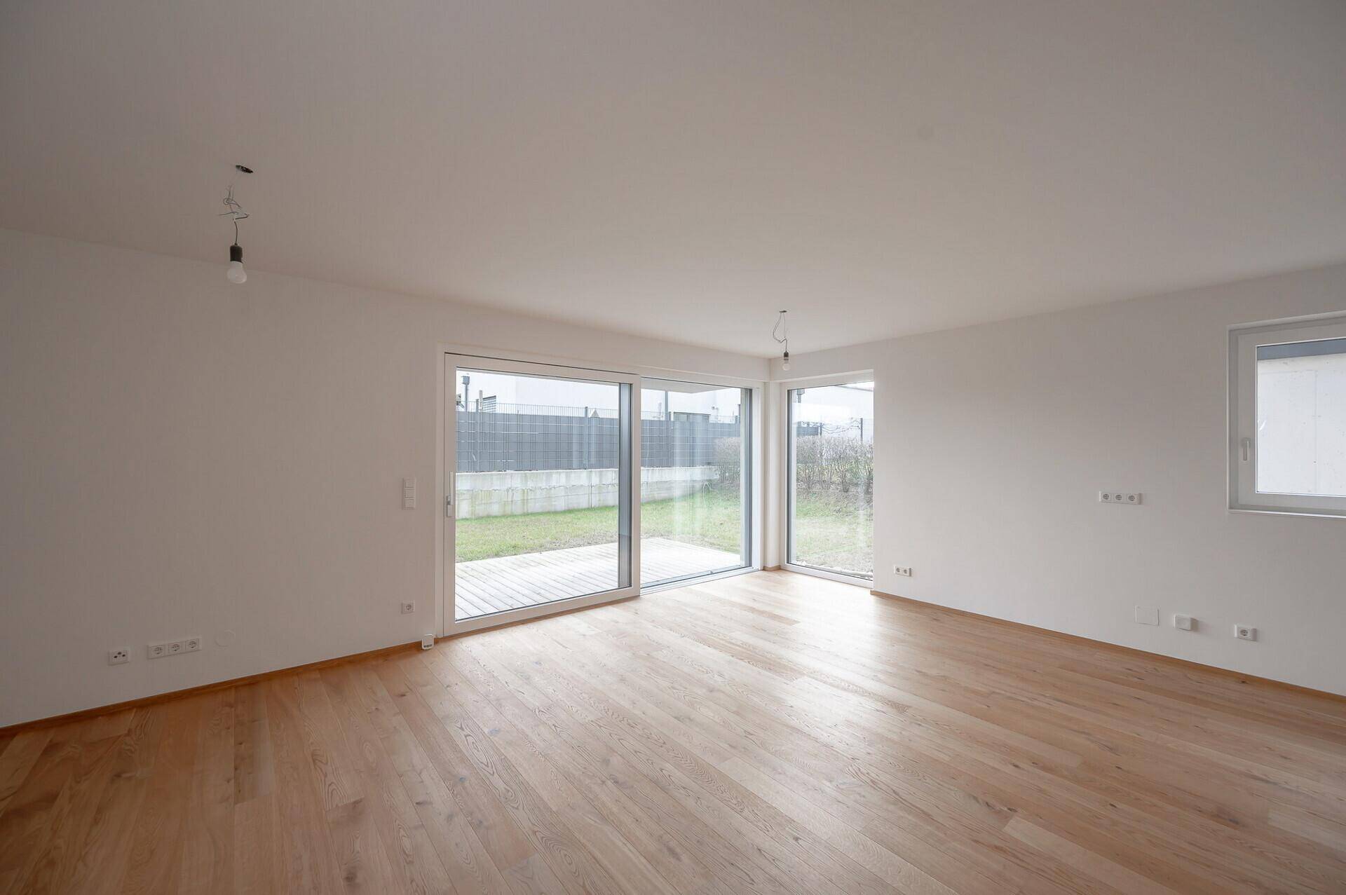 Lichtdurchflutetes Wohnzimmer mit Eichenparkett und breiter Schiebetür zur Terrasse.