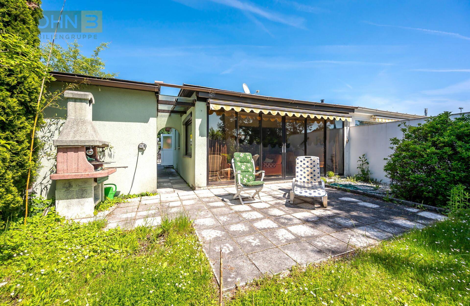 Gepflasterte Terrasse mit Liegestühlen und festem Grillplatz hinter dem Haus.
