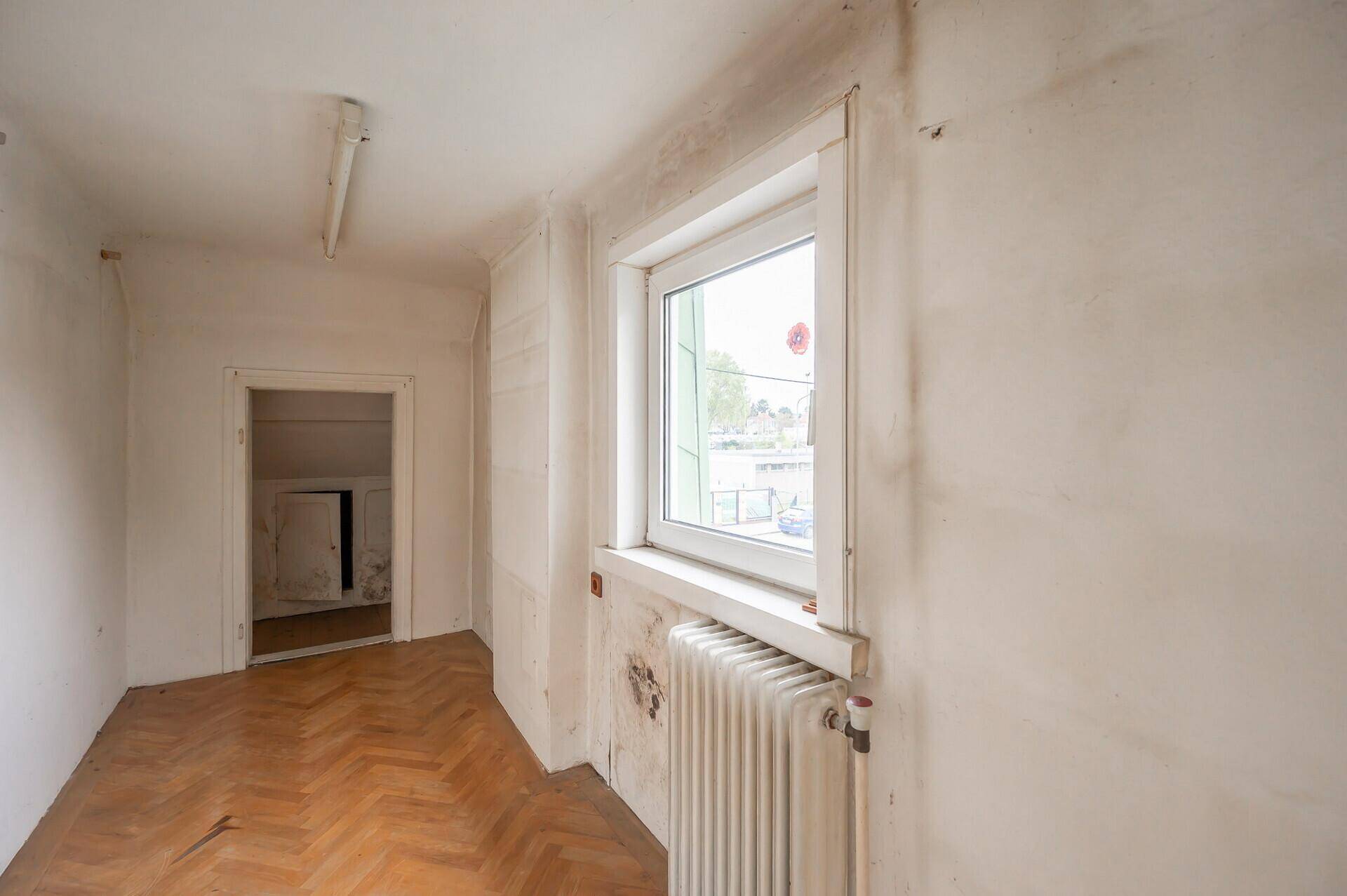 Helles Zimmer mit Holzboden, Fenster und Heizkörper, ideal als Schlaf- oder Arbeitszimmer.