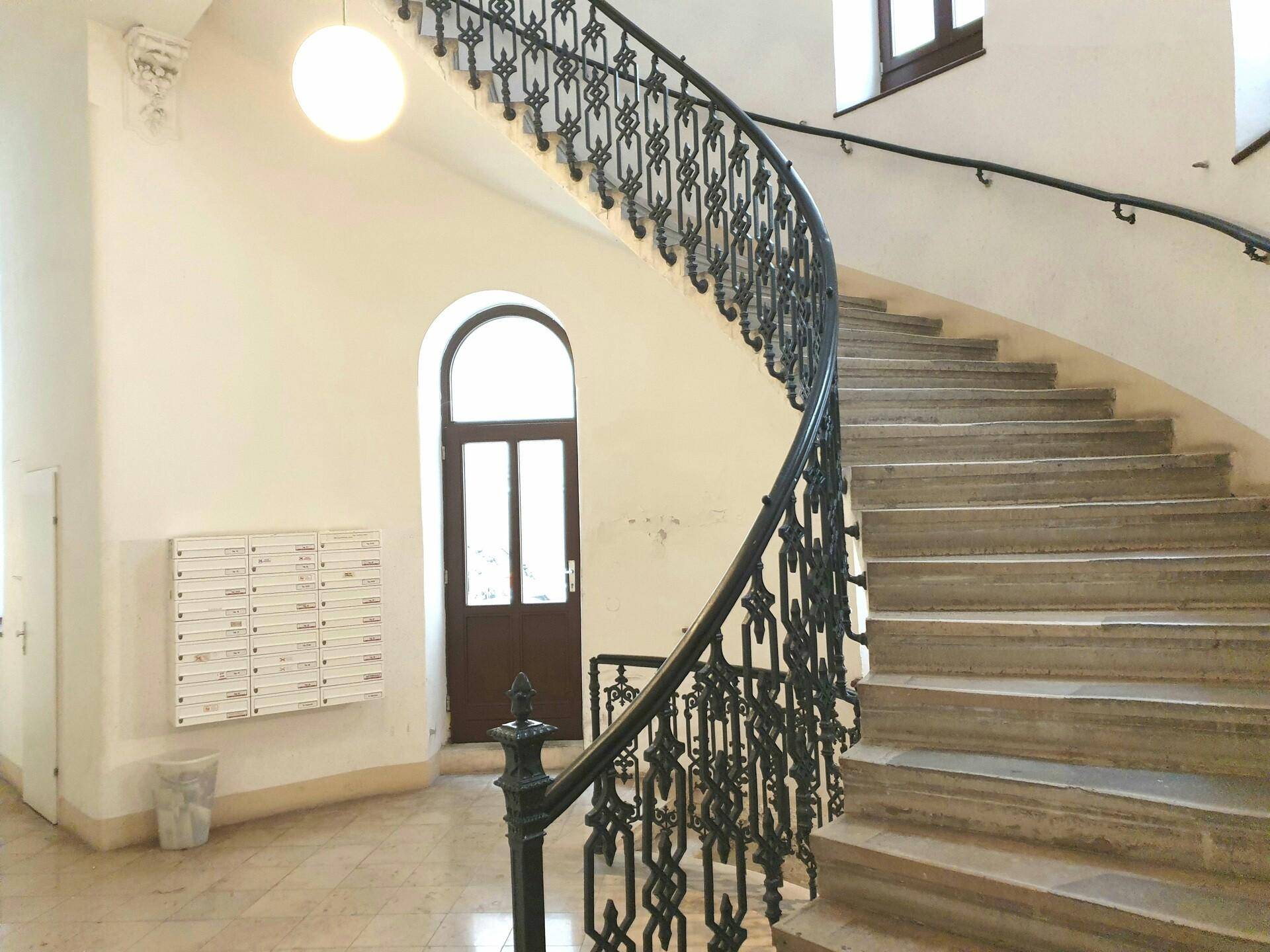 Elegantes Treppenhaus mit geschwungenem schmiedeeisernem Geländer und Marmorboden im Eingangsbereich.