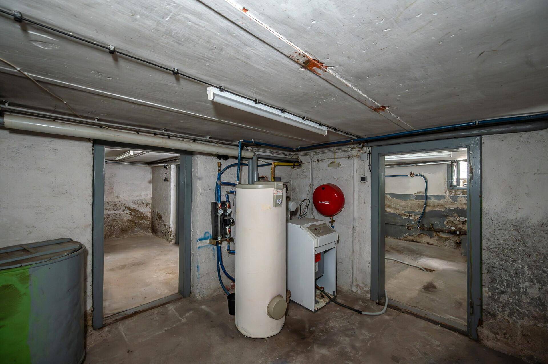Kellerraum mit Heizungsanlage, Warmwasserspeicher und freiliegenden Rohren.
