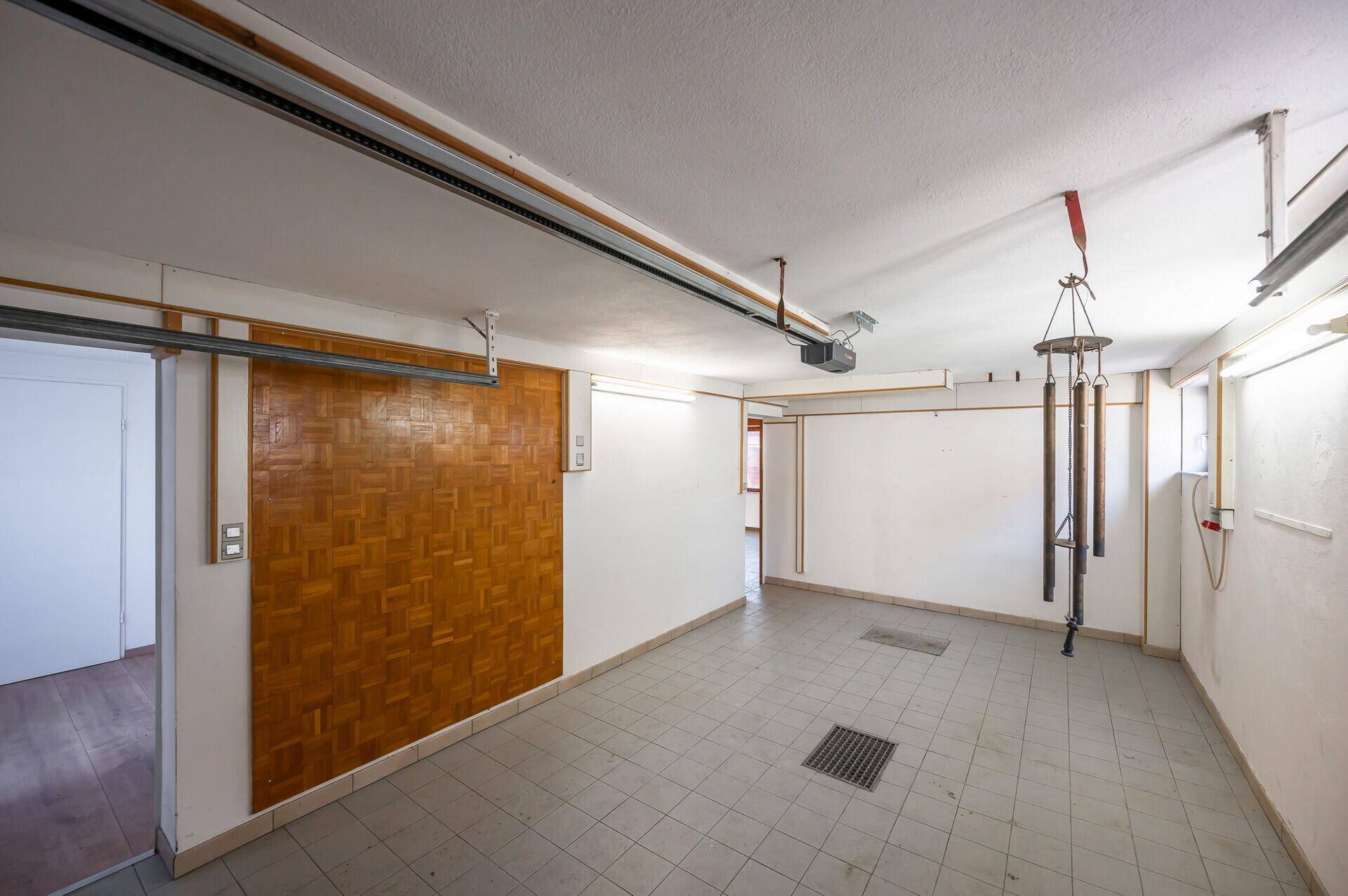 Geräumige Garage mit Fliesenboden und Holzwandverkleidung, bereit für Fahrzeuge oder Lagerung.