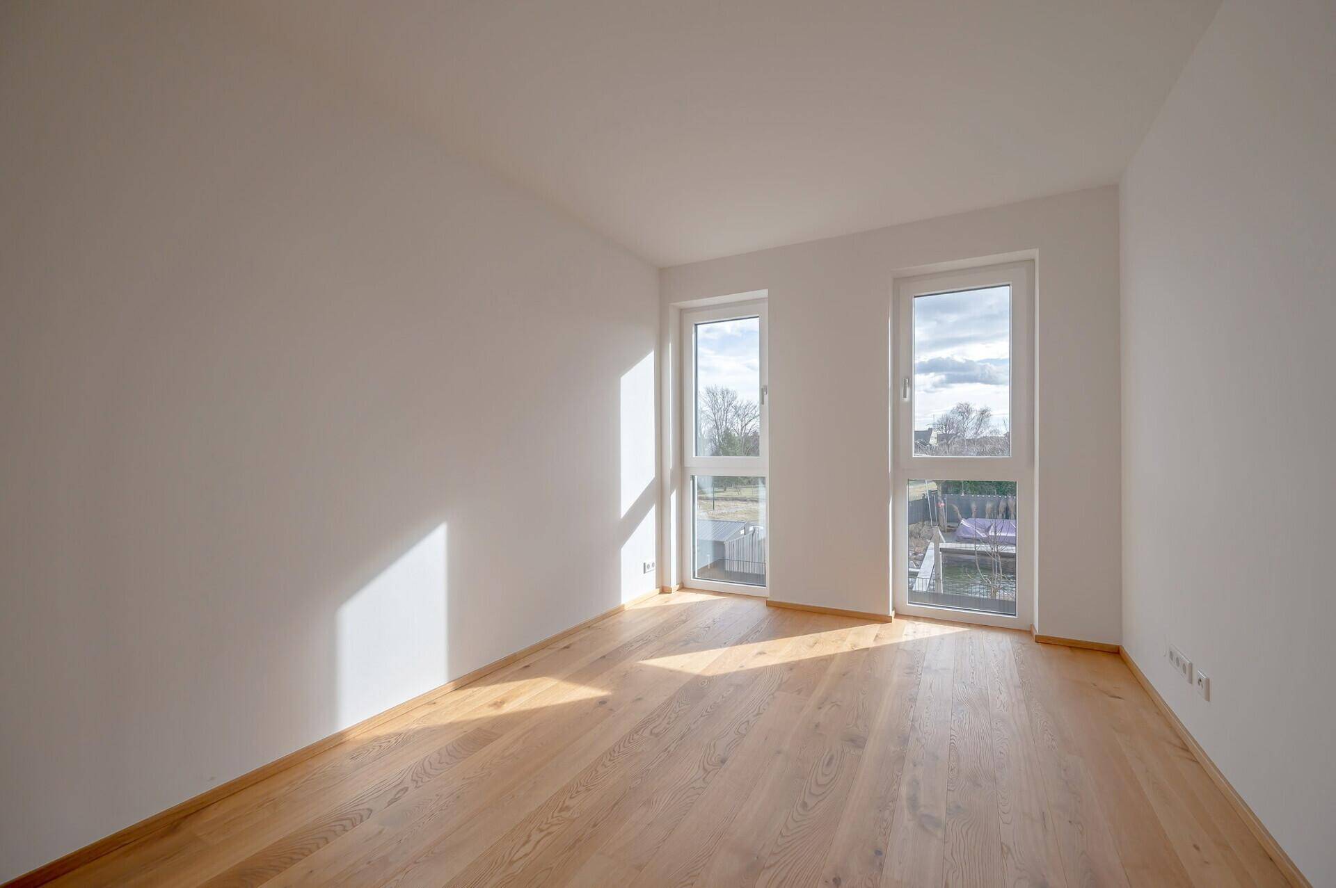 Sonniger Schlafbereich mit Eichenparkett und zwei Fenstern, die viel Licht hereinlassen.