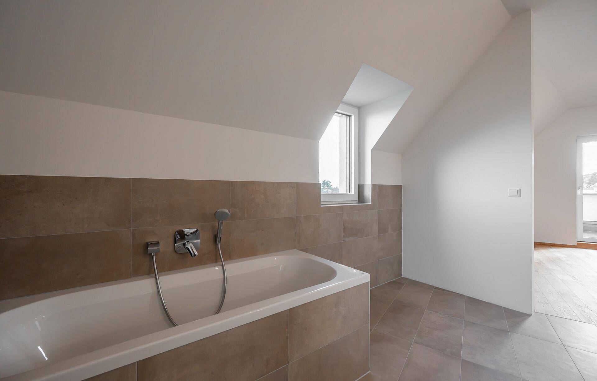Modernes Badezimmer im Dachgeschoss mit Badewanne und Fliesenboden.