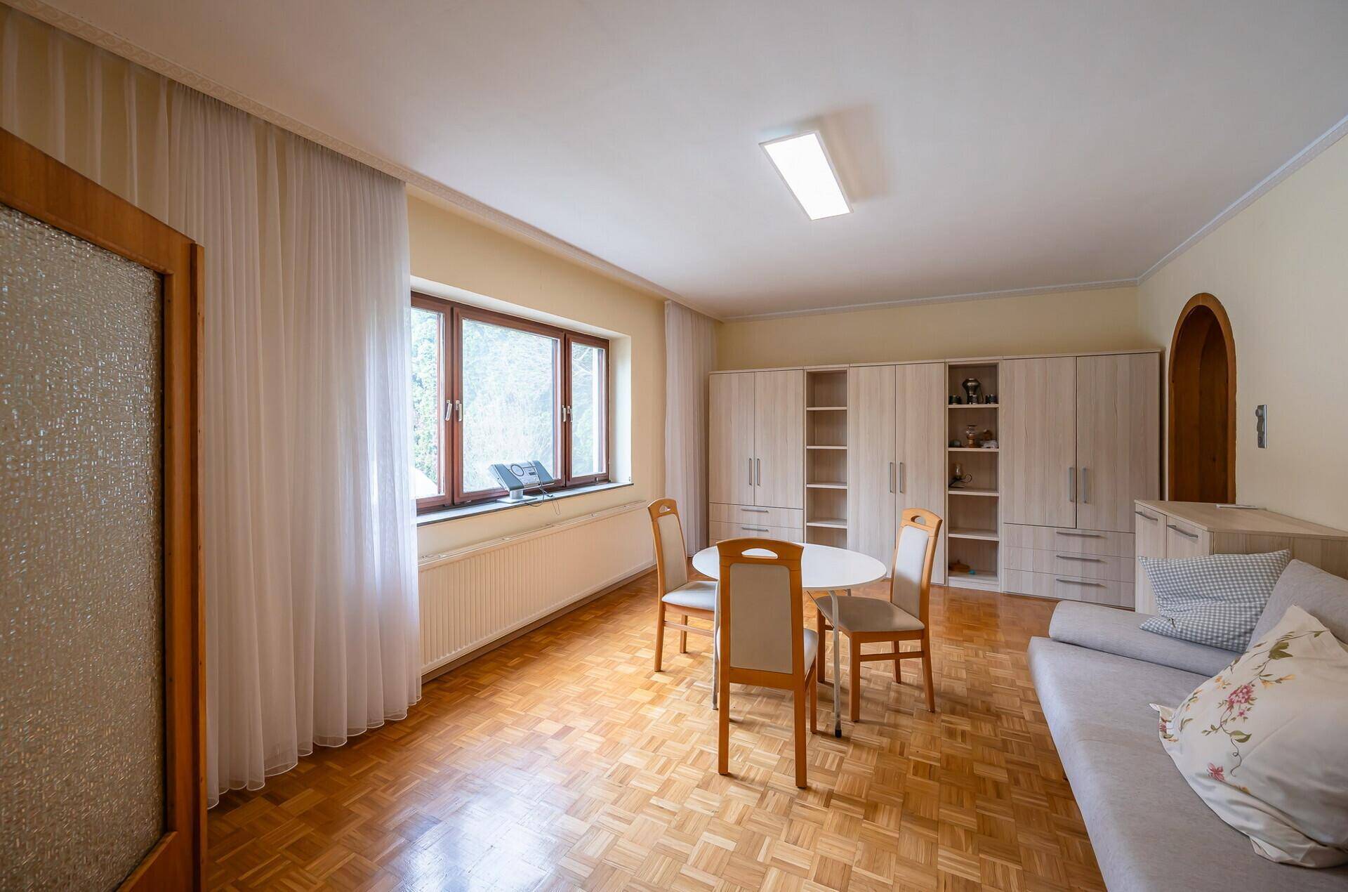 Geräumiger Wohn-Essbereich mit Parkettboden, großem Fenster und integrierten Schränken.