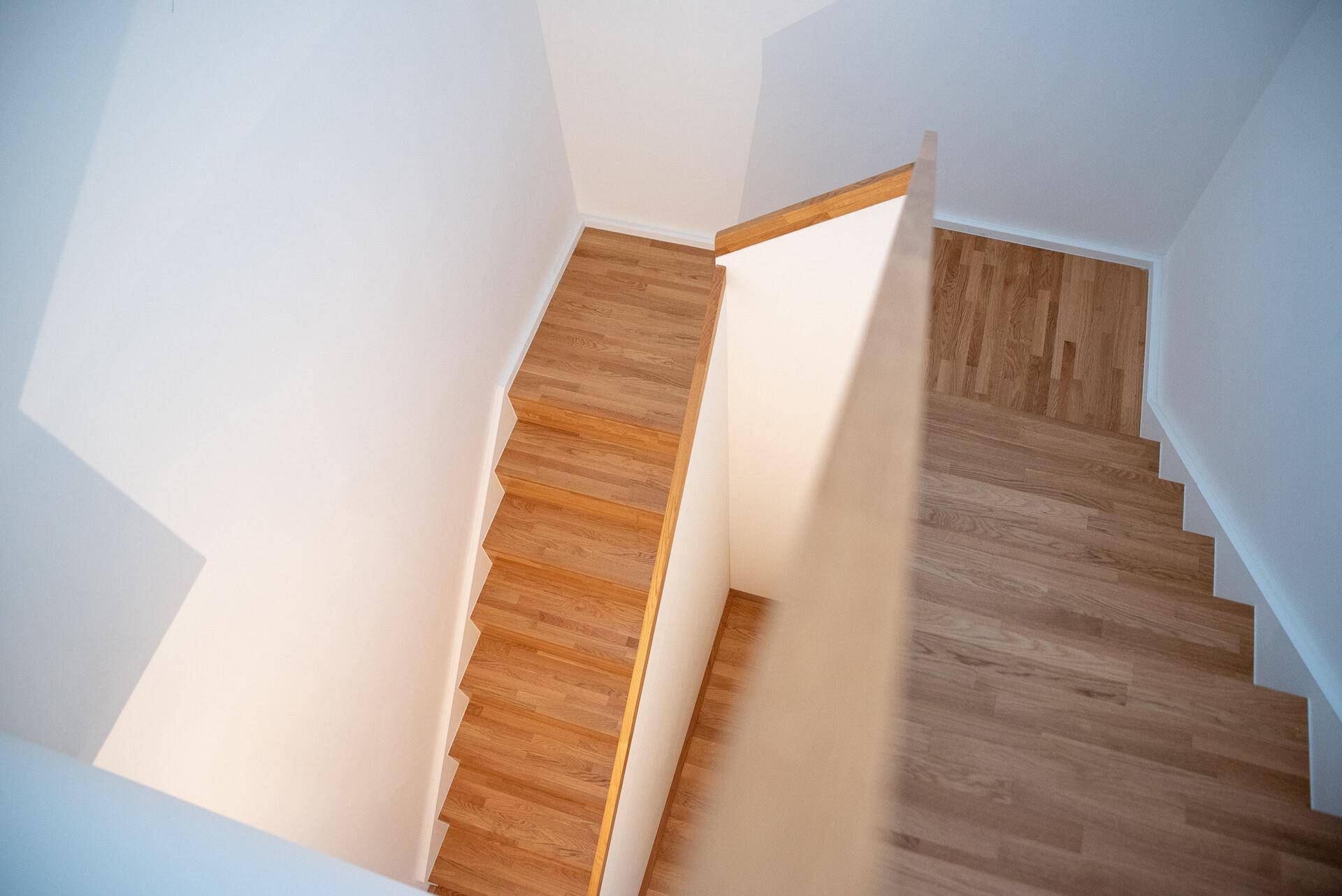 Moderne Holztreppe mit hellem Geländer, die die verschiedenen Ebenen der Wohnung verbindet.