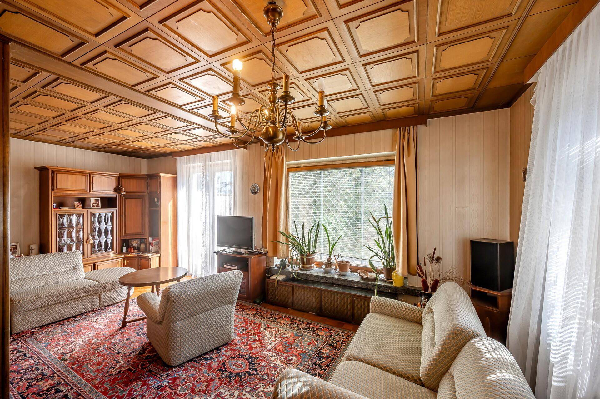 Gemütliches Wohnzimmer mit Holzkassettendecke, Teppich und traditionellen Möbeln.