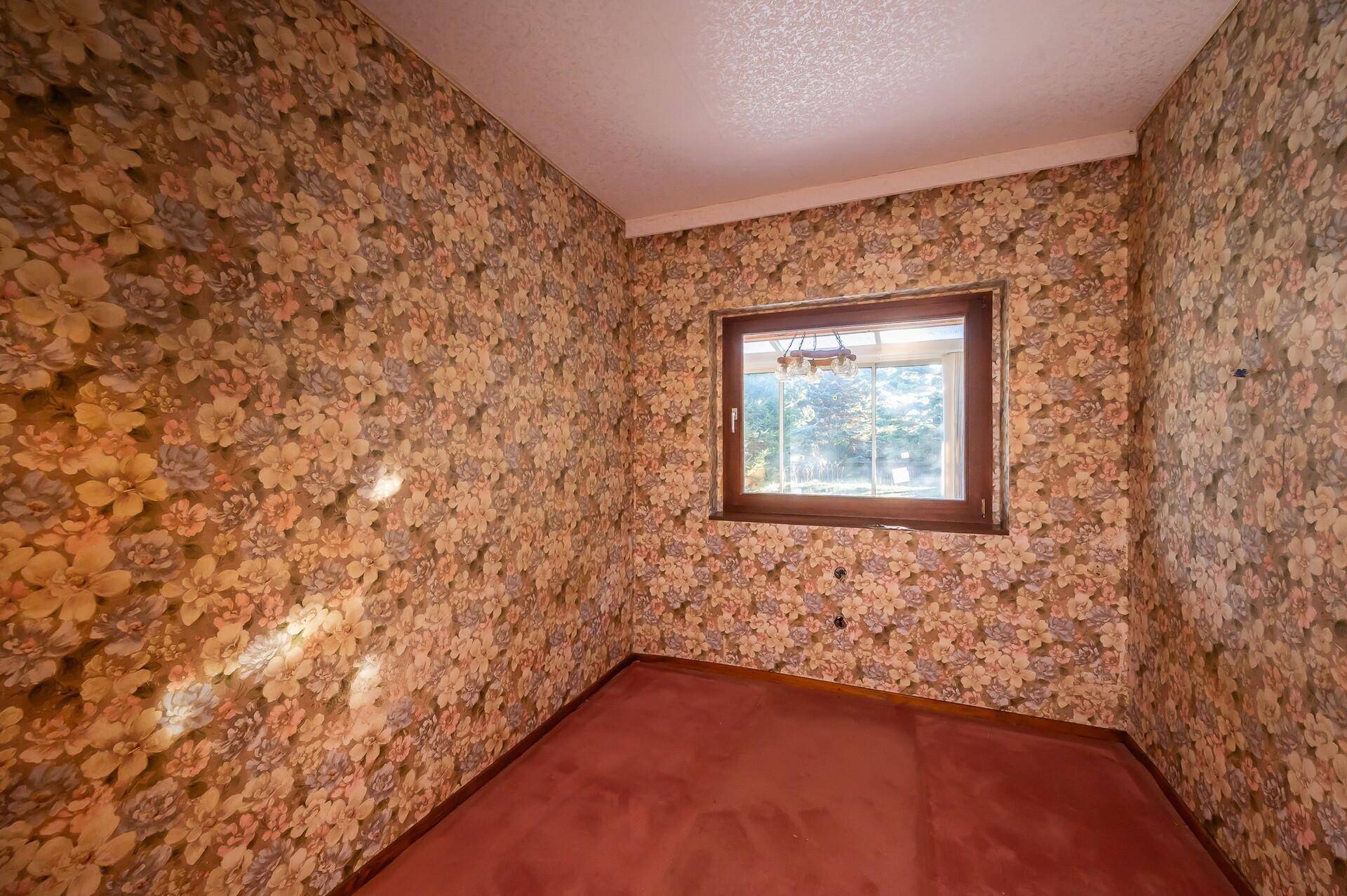 Schlafzimmer mit floraler Tapete und Teppichboden, bietet einen Blick ins Grüne.