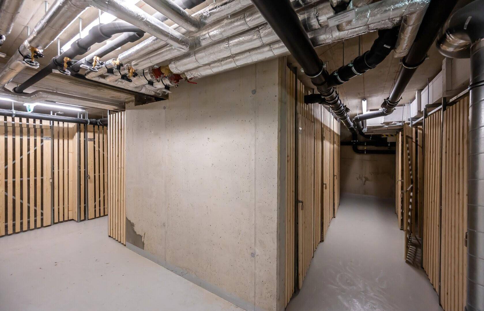 Kellerabteil mit sichtbaren Rohren und Holzabtrennungen für Stauraum.