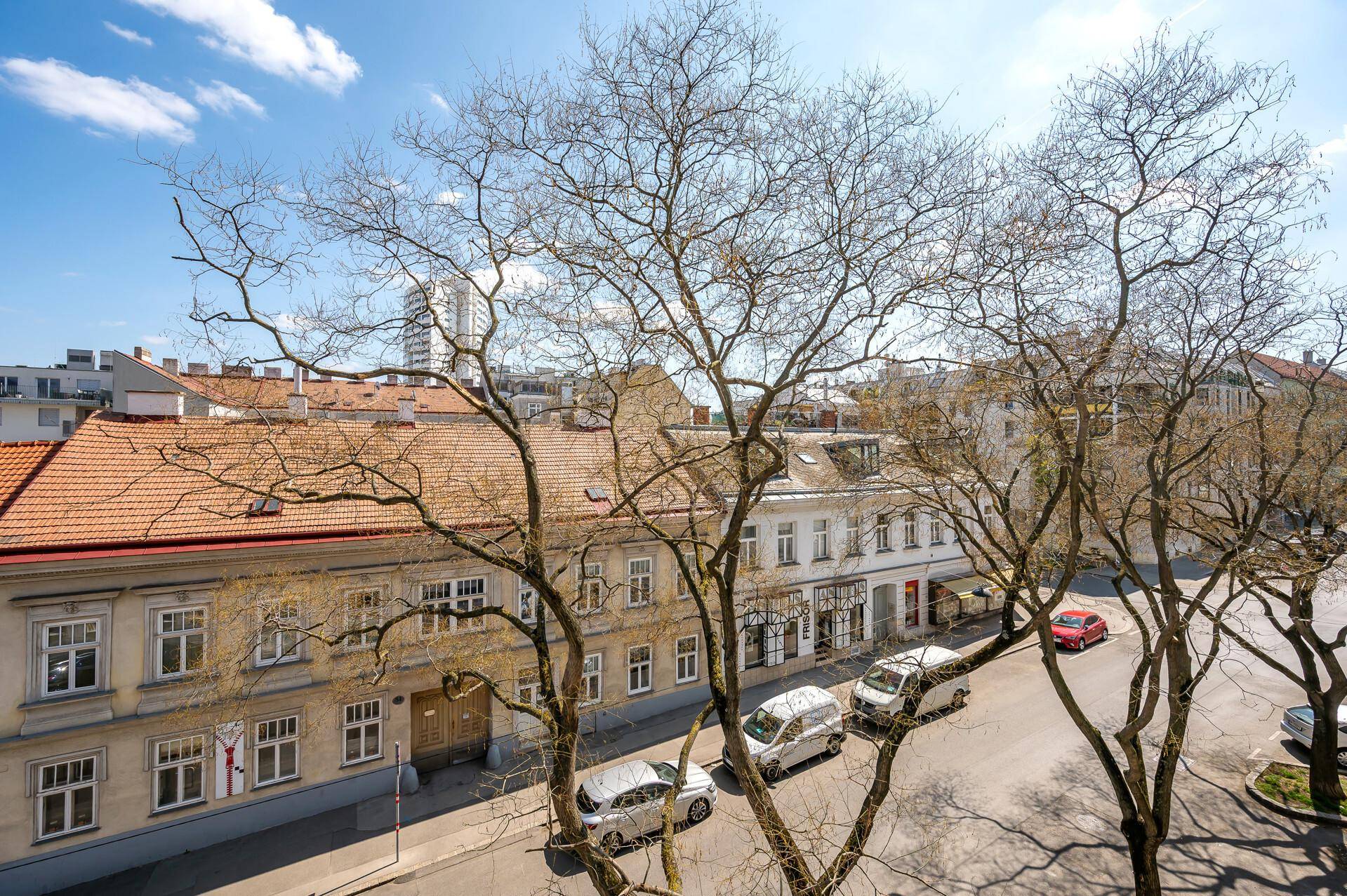 Straßenansicht von einem oberen Stockwerk mit Bäumen, parkenden Autos und traditionellen Gebäuden.