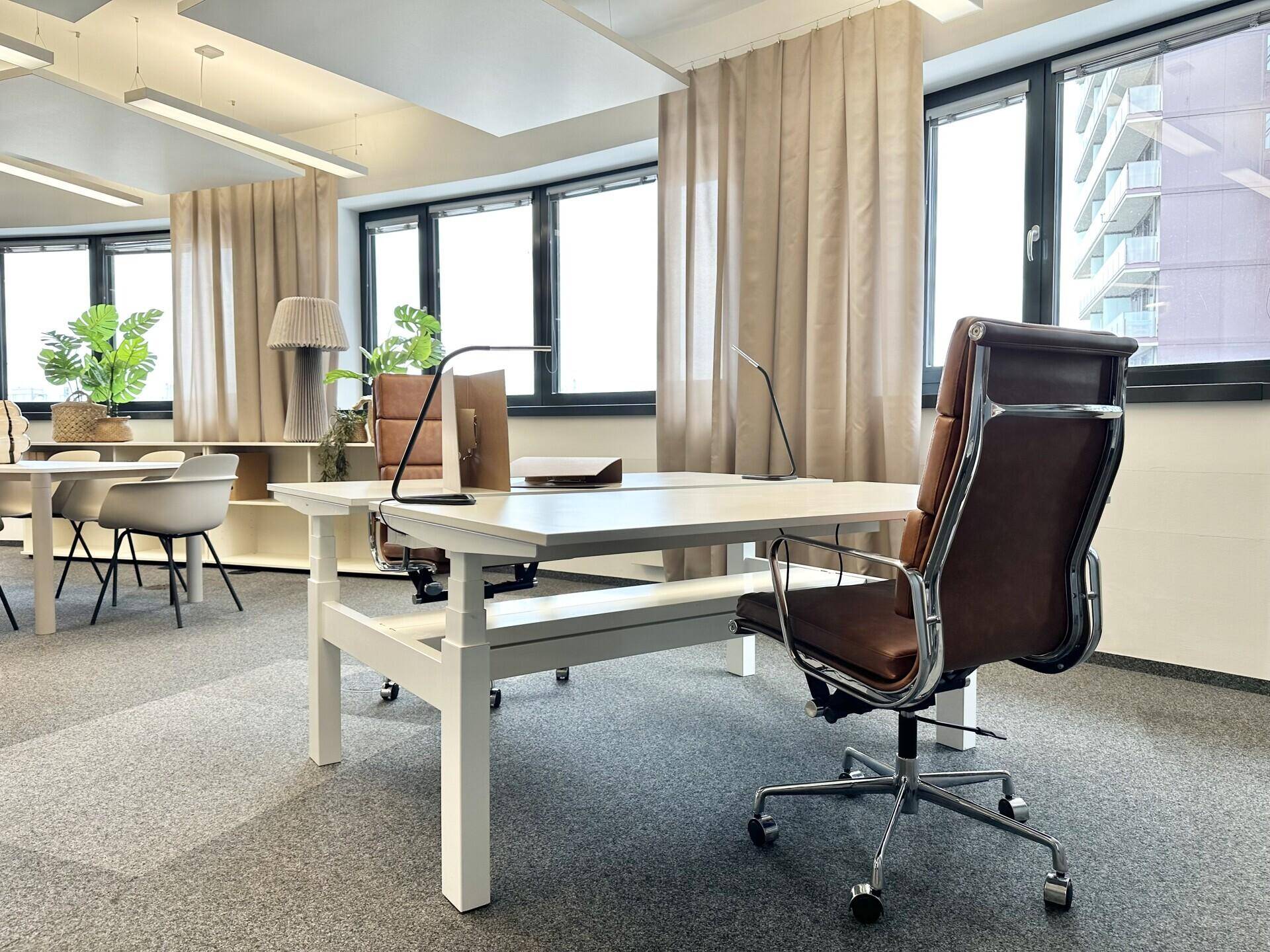 Moderner Arbeitsplatz mit ergonomischem Bürostuhl und Schreibtisch, umgeben von großen Fenstern und Pflanzen.