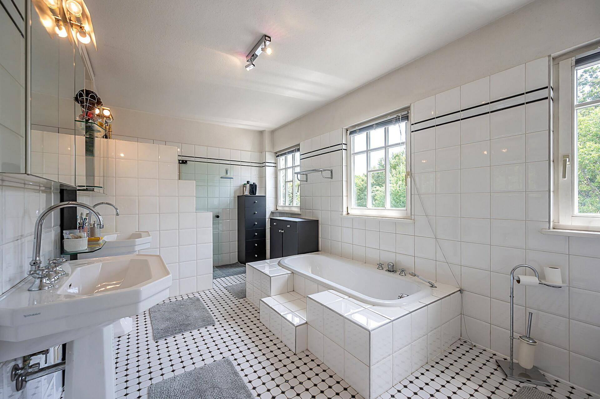 Geräumiges Badezimmer mit Badewanne, Dusche und schwarz-weißem Fliesenboden.