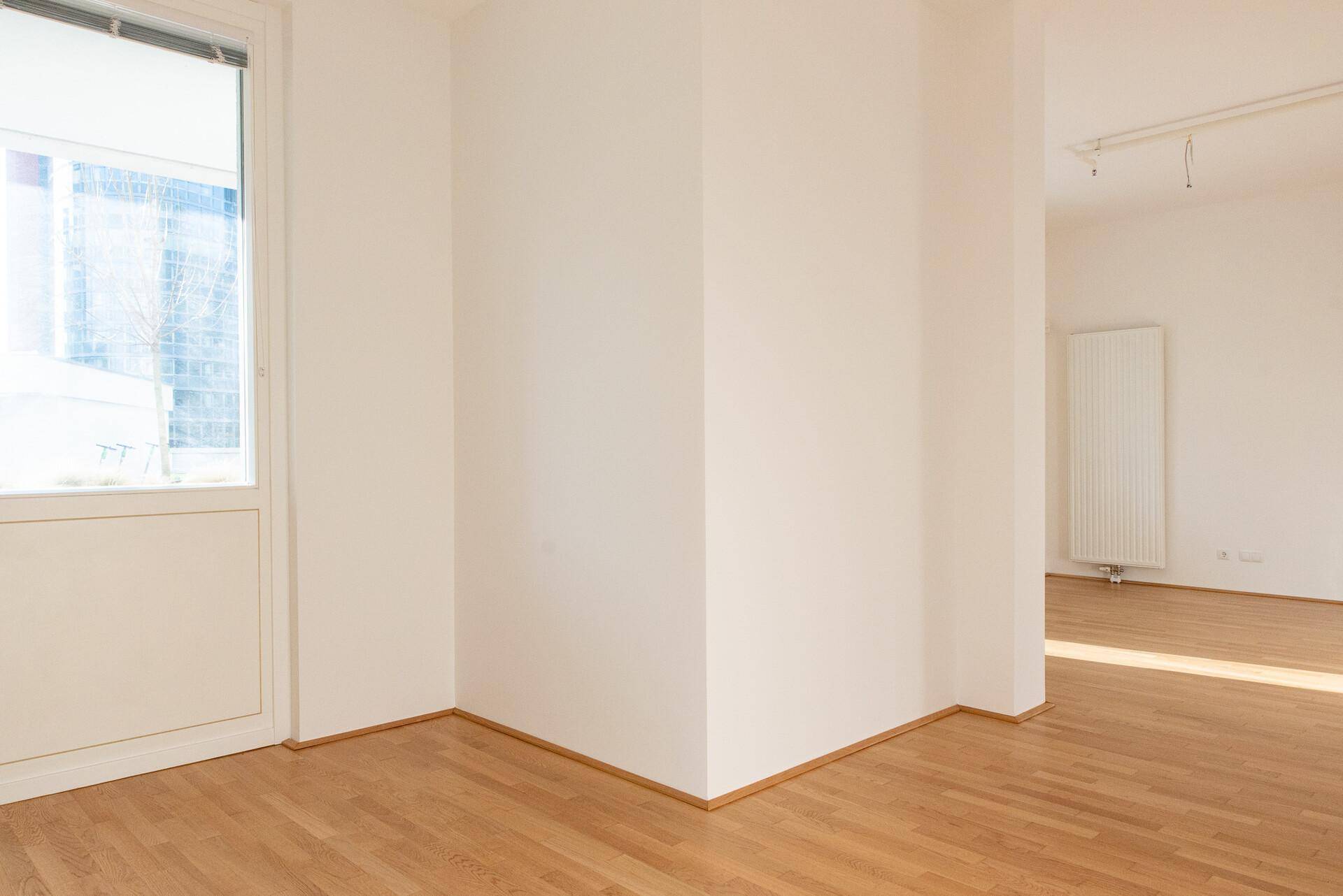 Heller Wohnbereich mit Holzboden und einem Fenster, das viel Tageslicht hereinlässt.
